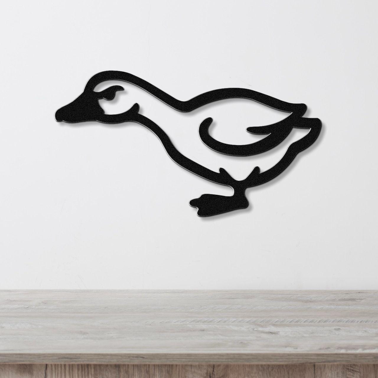 Black metal goose wall art silhouette with cutout details, mounted on a white wall above a light wood surface.