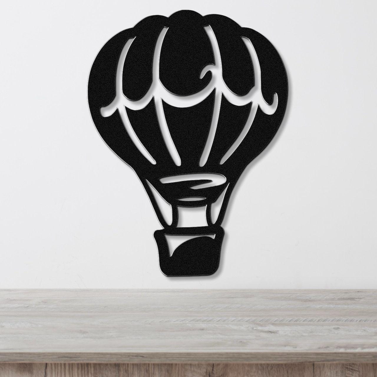 Black metal wall art in the silhouette of a hot air balloon with internal cutout details, mounted on a white wall above a light wood surface.