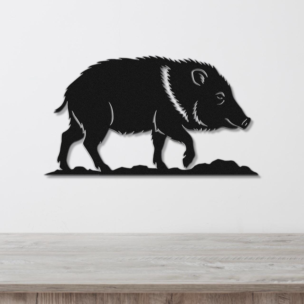 Black metal wall art silhouette of a javelina with detailed fur and facial features, mounted on a white wall above a wooden surface.