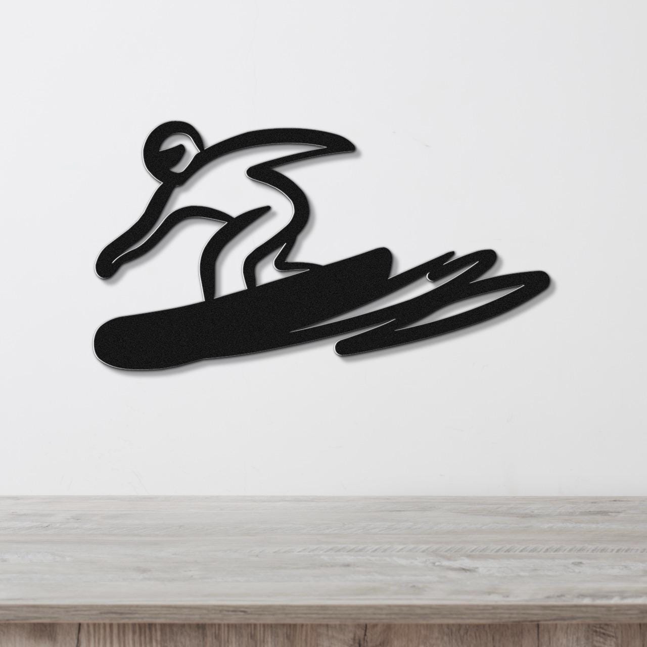 Black metal wall art featuring a bold silhouette of a snowboarder in motion, mounted on a white wall above a wooden surface.