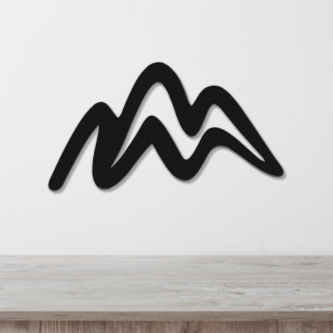 Black metal wall art with a wavy mountain silhouette, mounted on a white wall above a light wood surface.