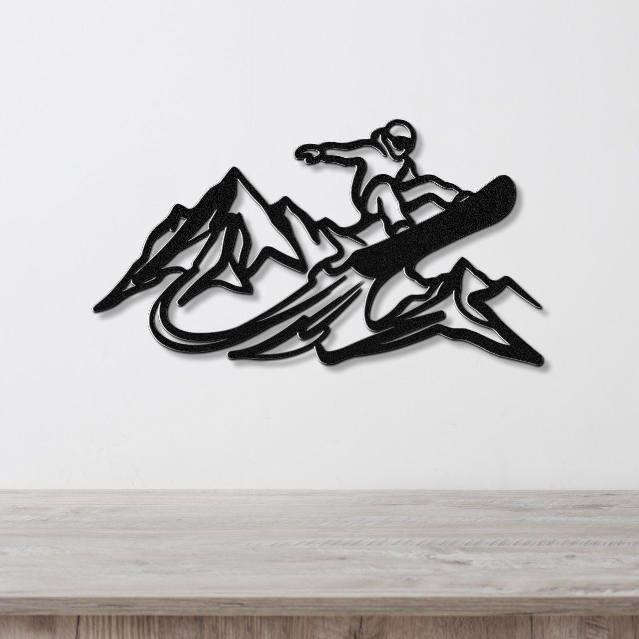 Black metal wall art featuring a snowboarder silhouette above mountain peaks, mounted on a white wall above a wooden counter.