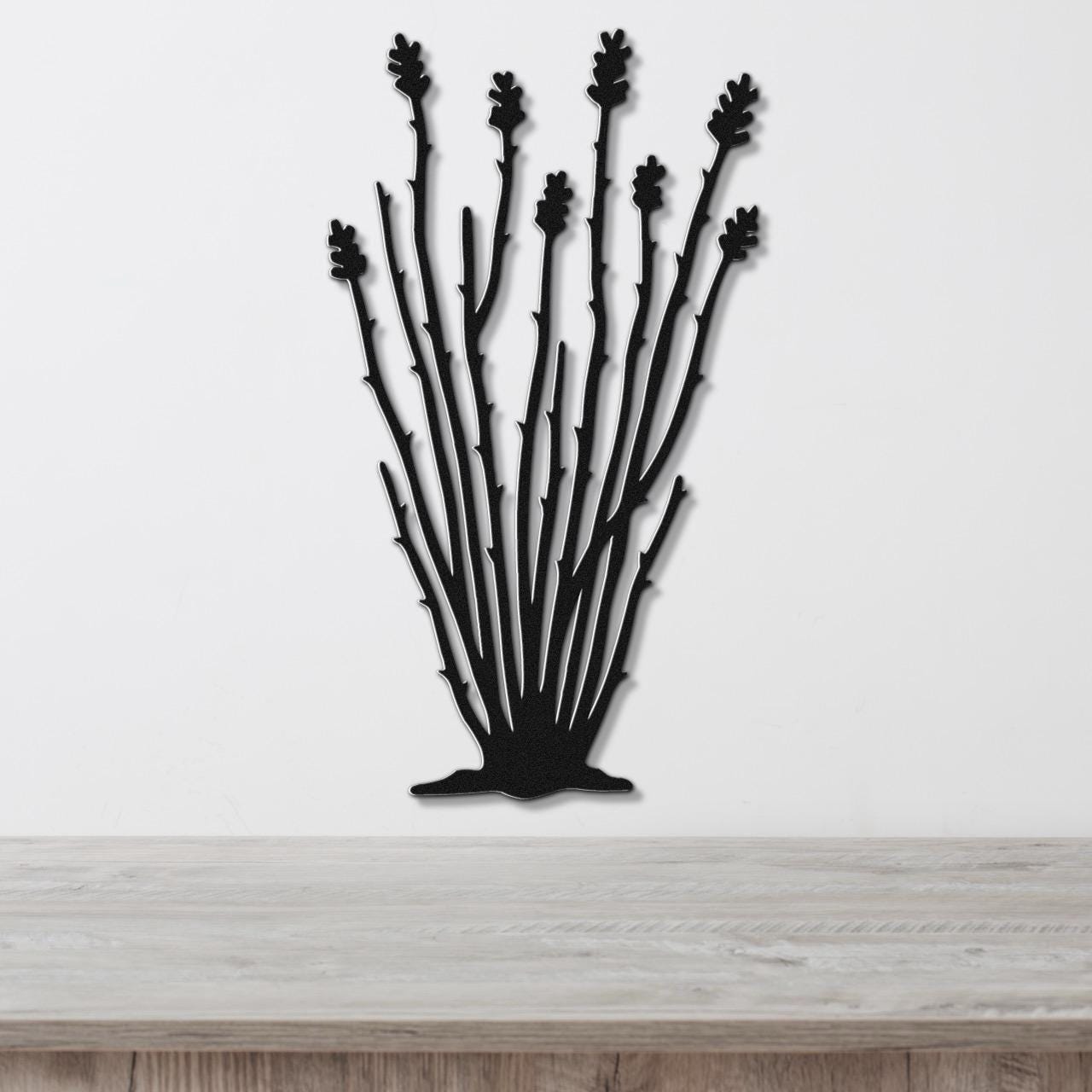 Black metal wall art cutout of an ocotillo plant with multiple spiny stems and leaf clusters, mounted on a white wall above a light wood surface.