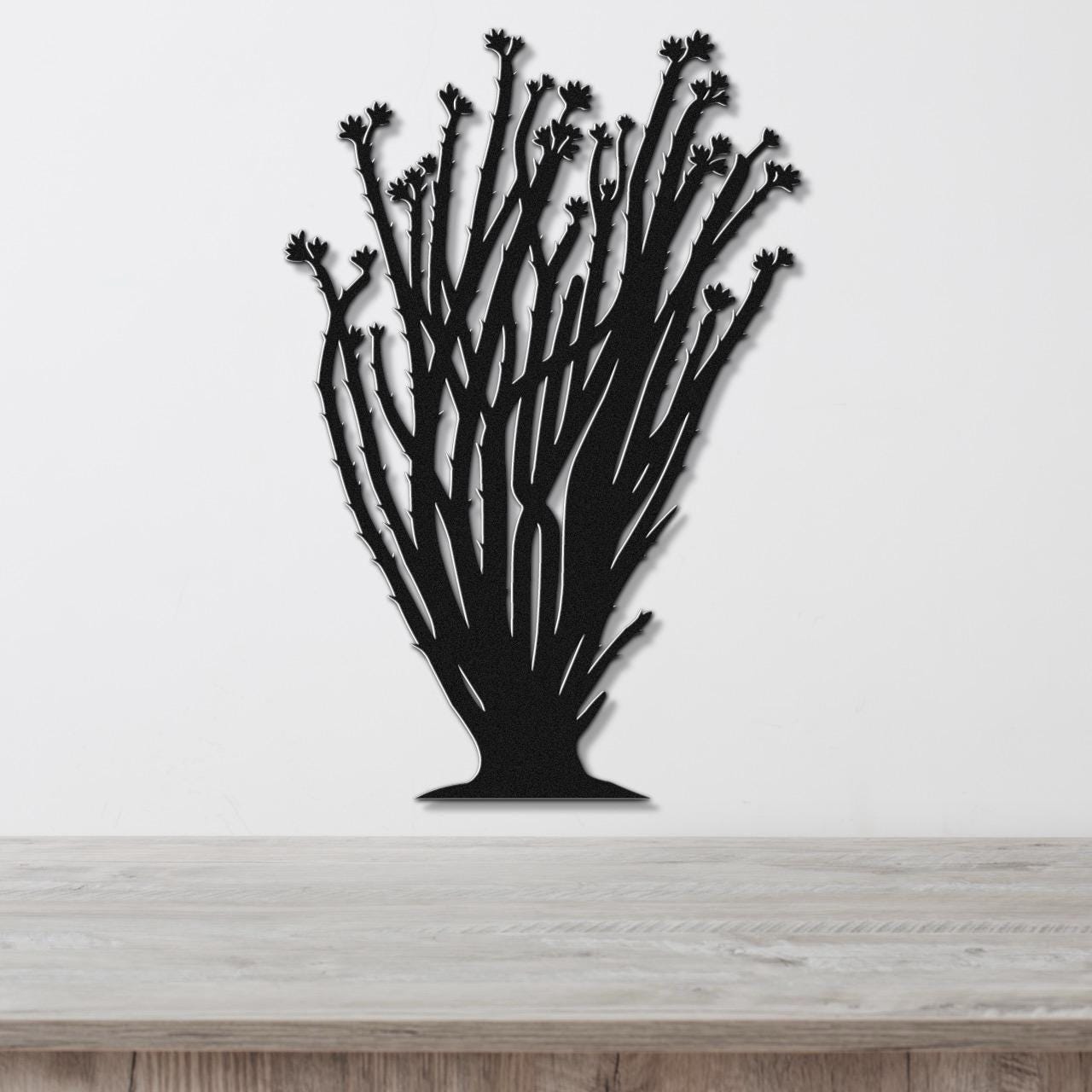 Black metal ocotillo wall art with branching stems and flower cutouts, mounted on a white wall above a wooden counter.