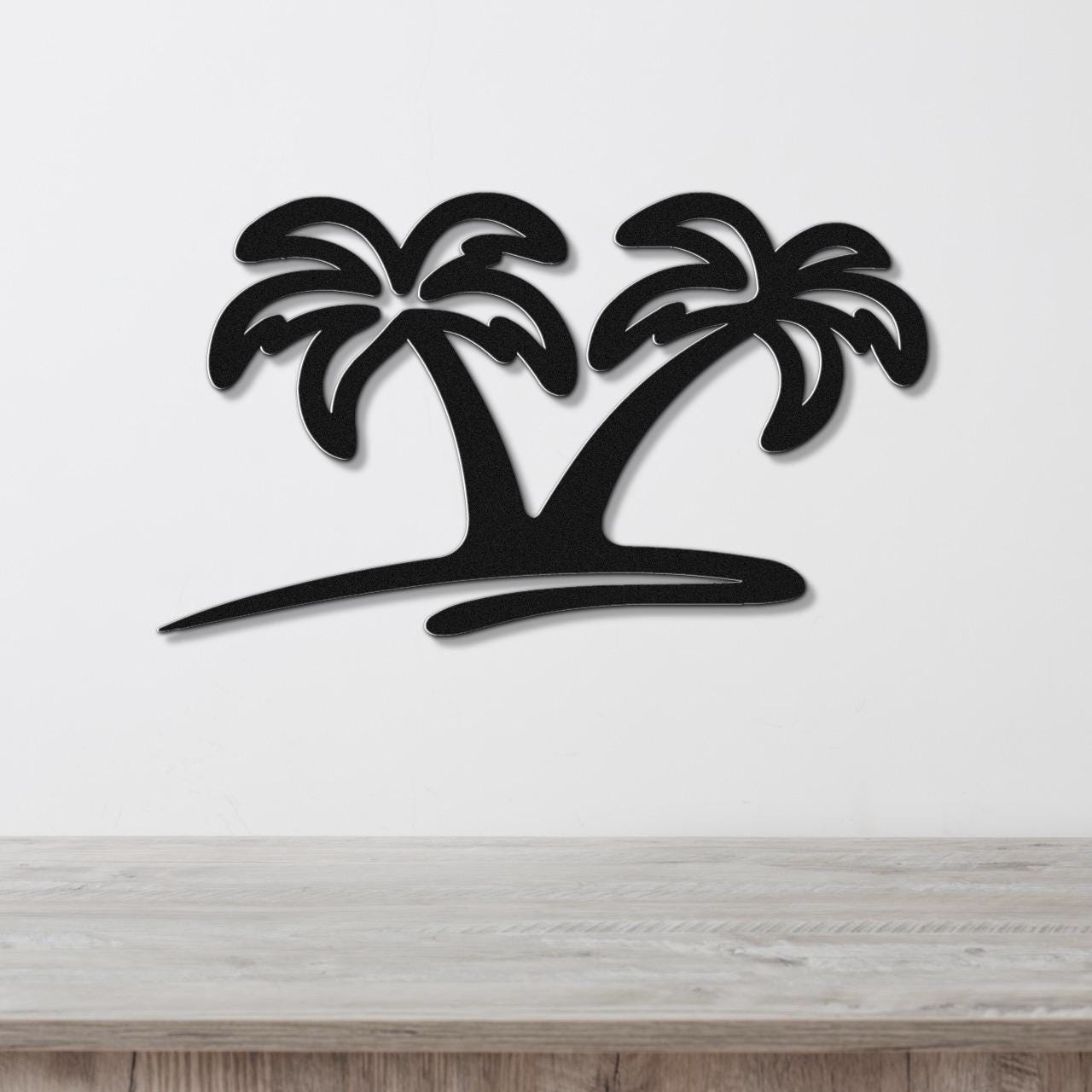 Black metal wall art featuring a silhouette of two palm trees with cutout fronds, mounted on a white wall above a wooden surface.