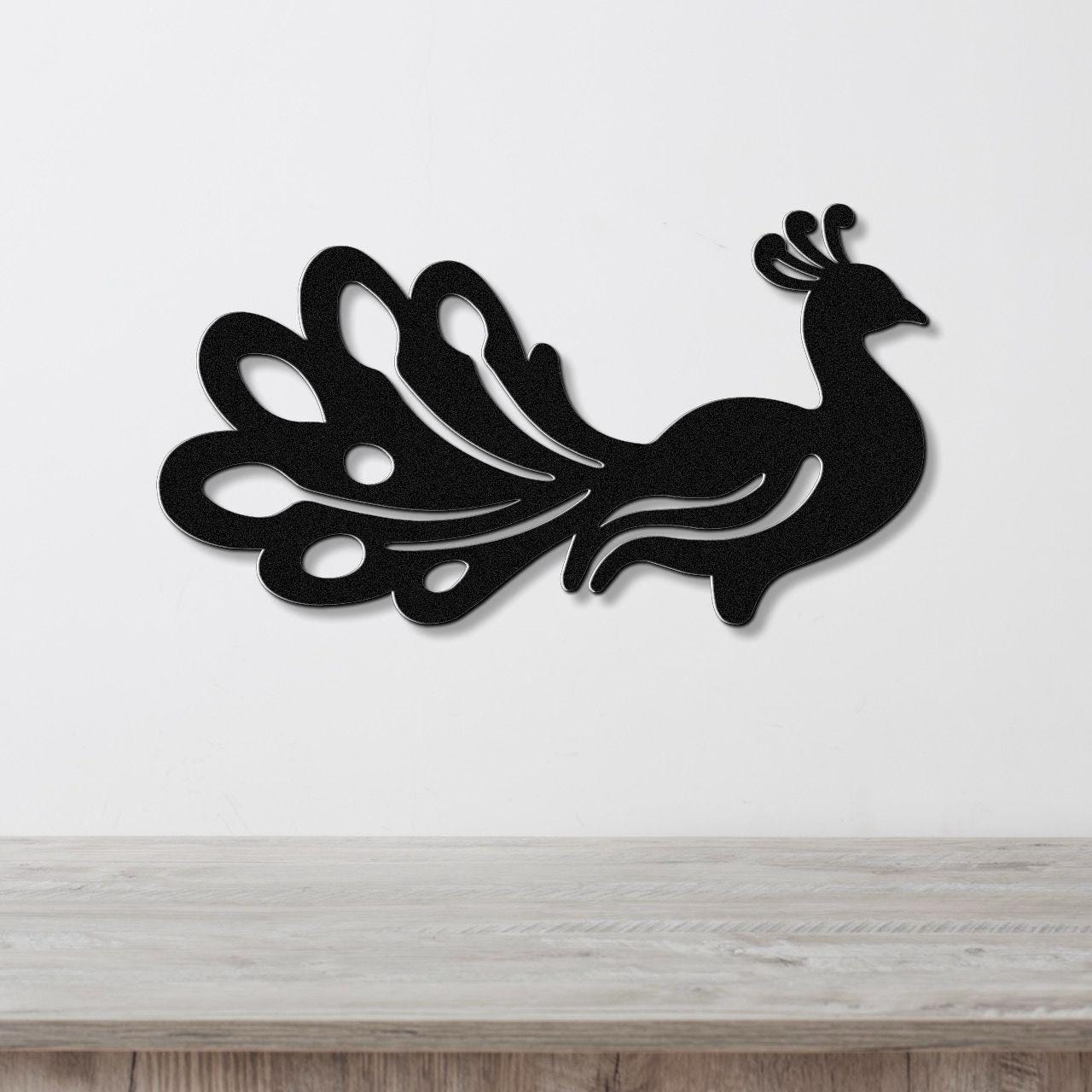 Black metal peacock wall art with a silhouette design and cutout tail feathers, mounted on a white wall above a wooden surface.