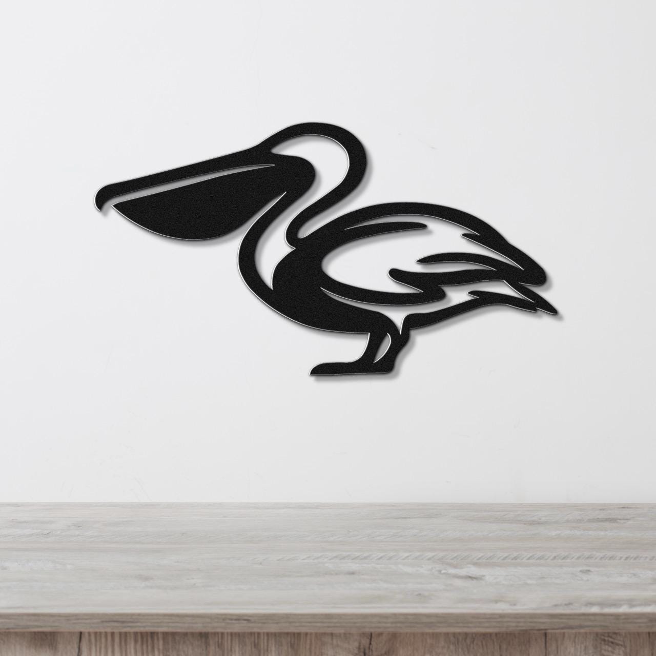 Black metal pelican wall art with a cutout silhouette design, mounted on a white wall above a light wood surface.
