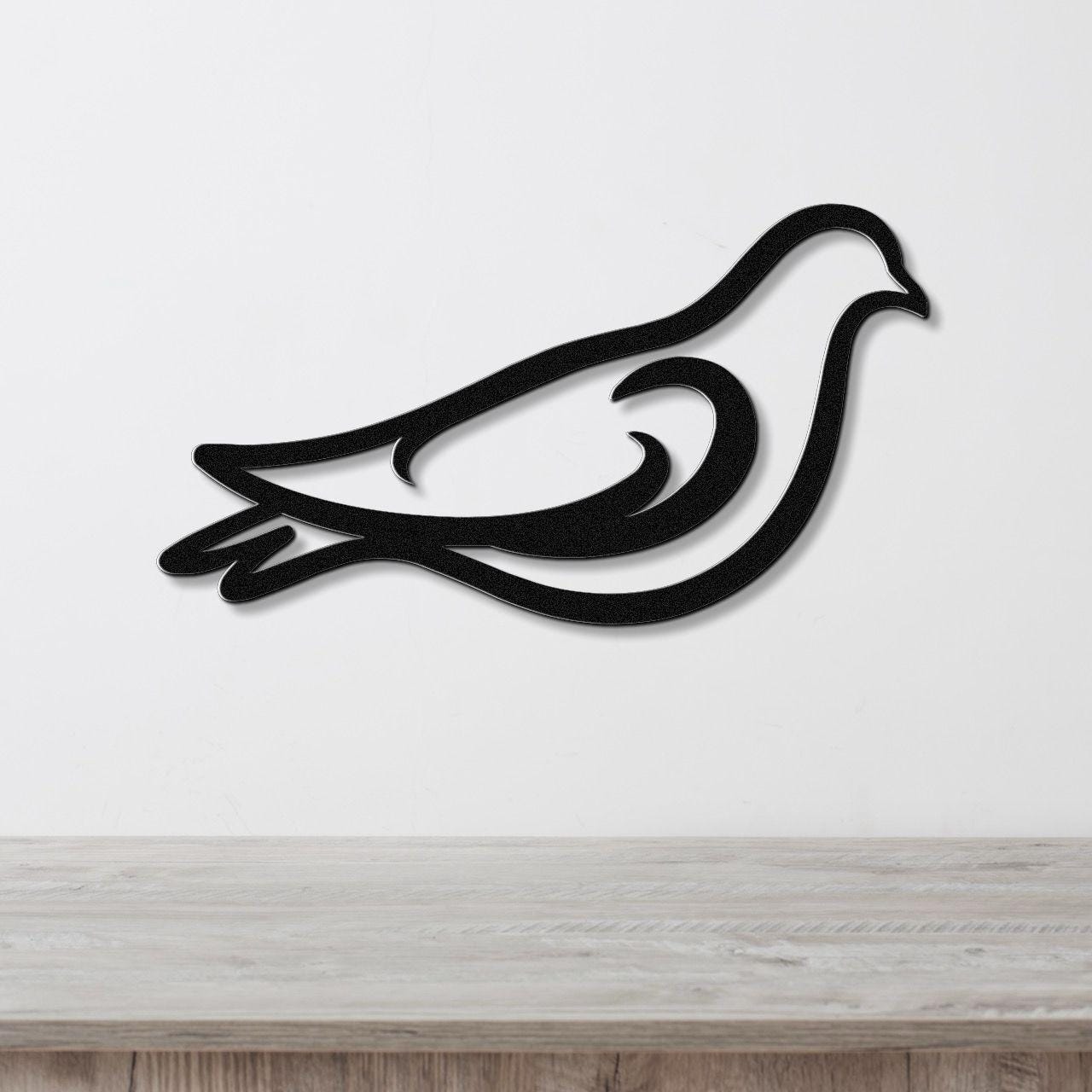 Black metal pigeon wall art with a bold silhouette and internal cutout details, mounted on a white wall above a light wood surface.