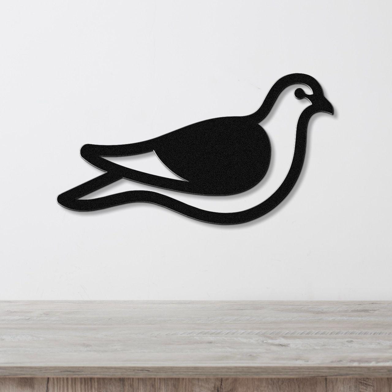 Black metal pigeon wall art with a cutout silhouette design, mounted on a white wall above a light wood surface.