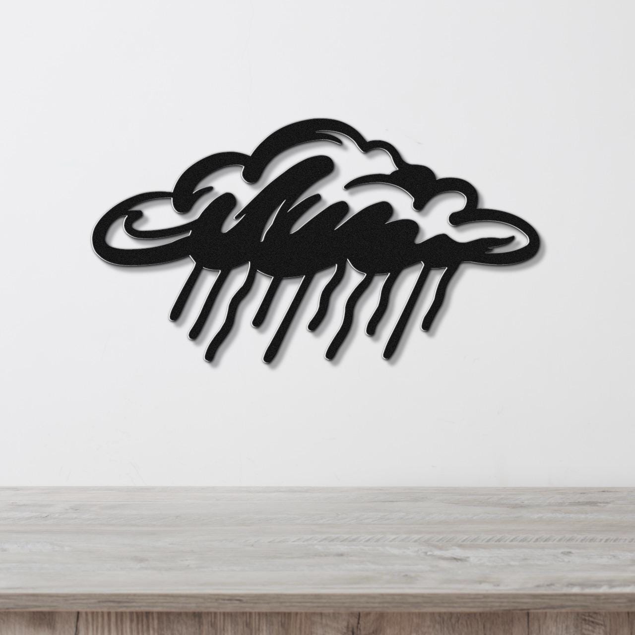 Black metal wall art in a cloud shape with raindrop cutouts, mounted on a white wall above a wooden surface.