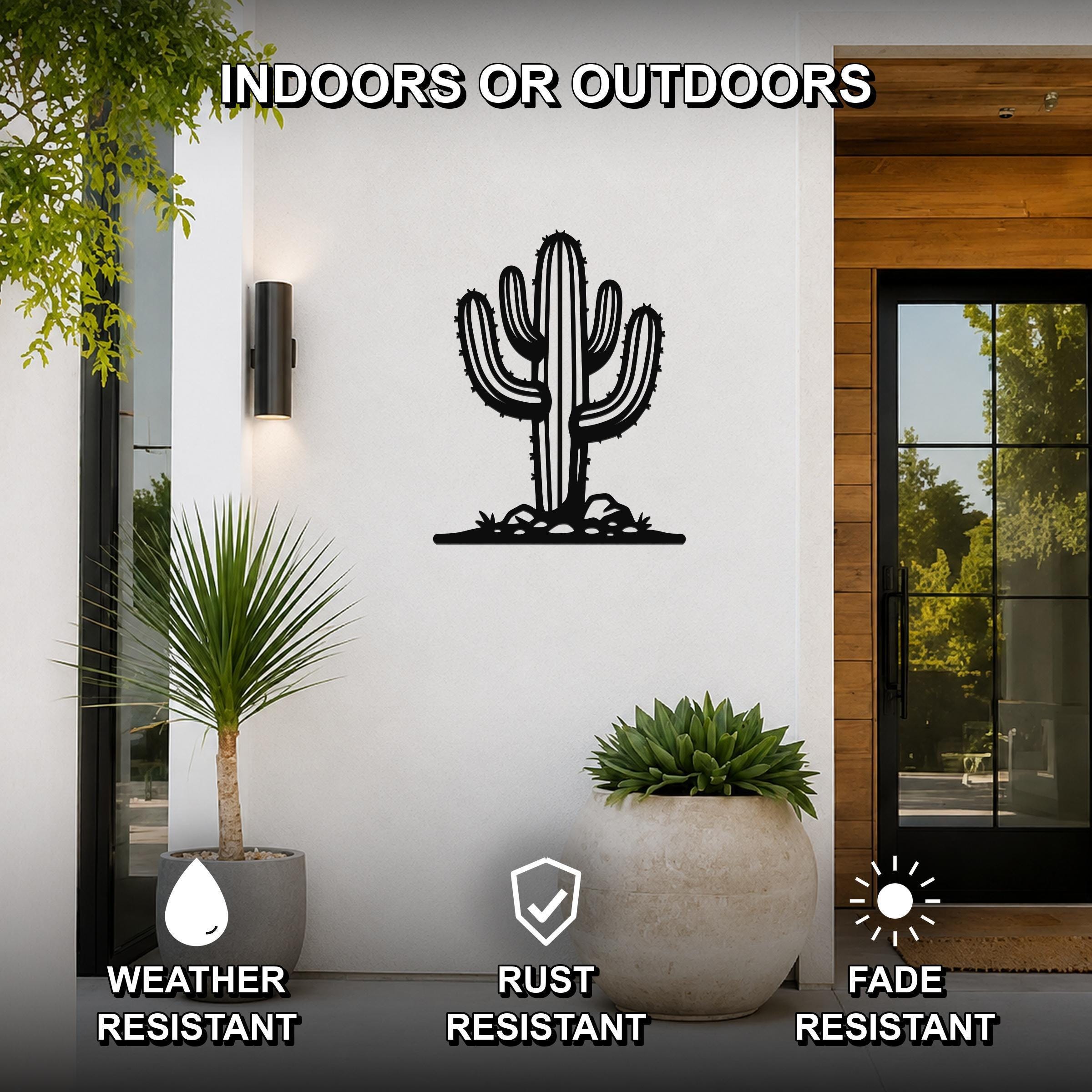 Black metal saguaro cactus wall art with spines and base cutouts, mounted on a white exterior wall beside a glass door and potted plants.
