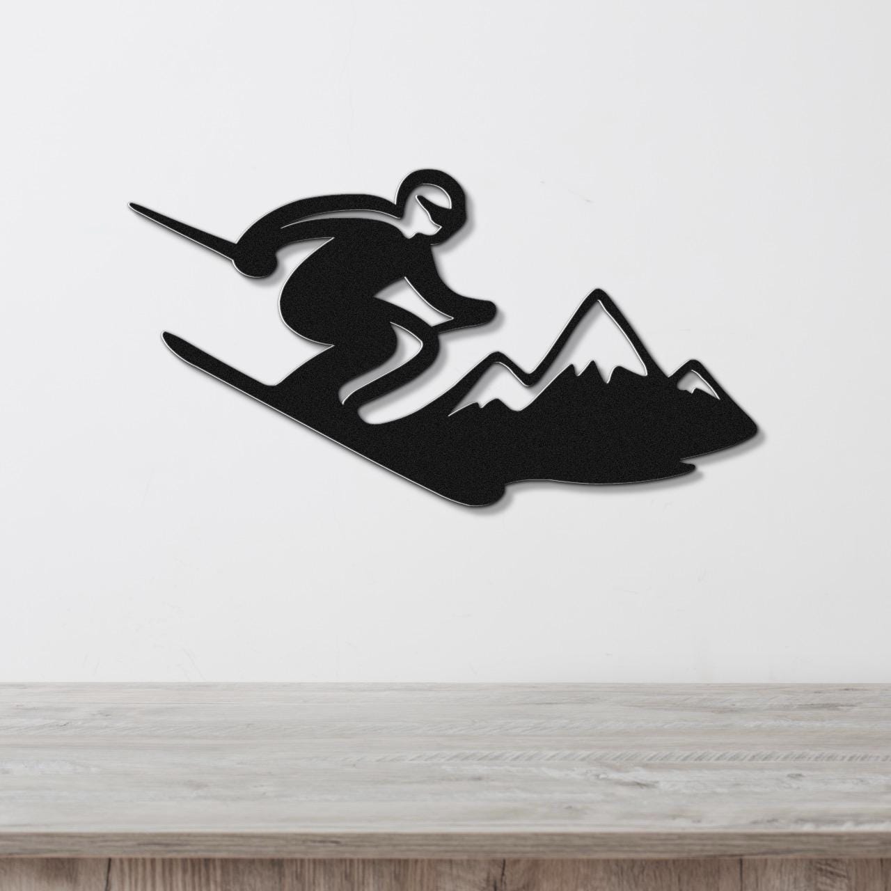 Black metal wall art silhouette of a skier in motion above a mountain range, mounted on a white wall above a wooden counter.