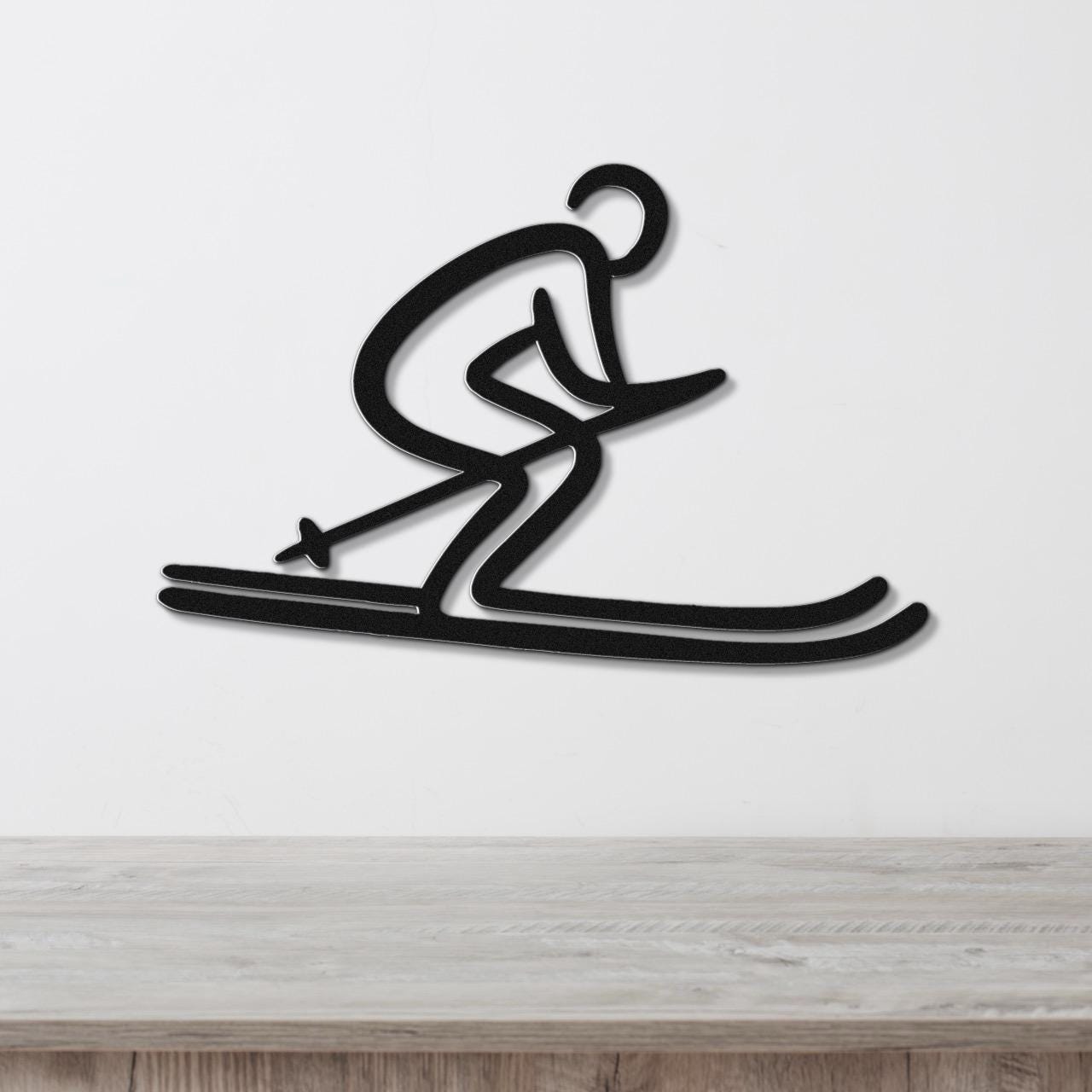 Black metal wall art of a dynamic skier silhouette with cutout details, mounted on a white wall above a light wood surface.