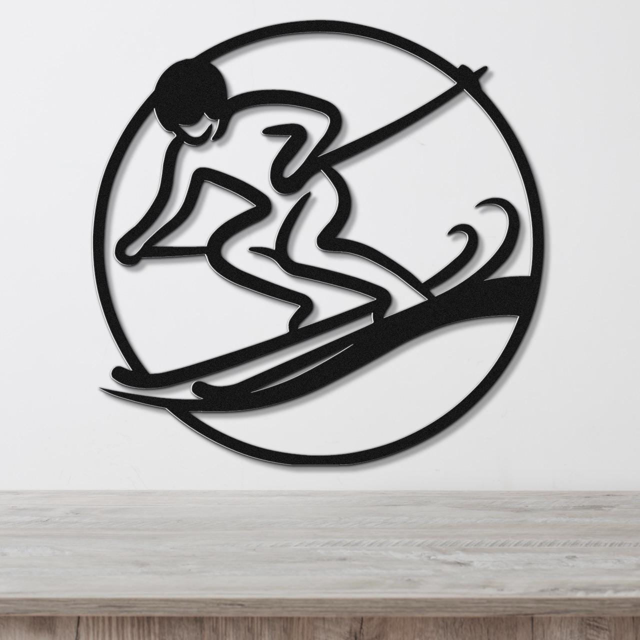 Black metal wall art featuring a skier silhouette in a circular frame with motion lines, mounted on a white wall above a wooden surface.