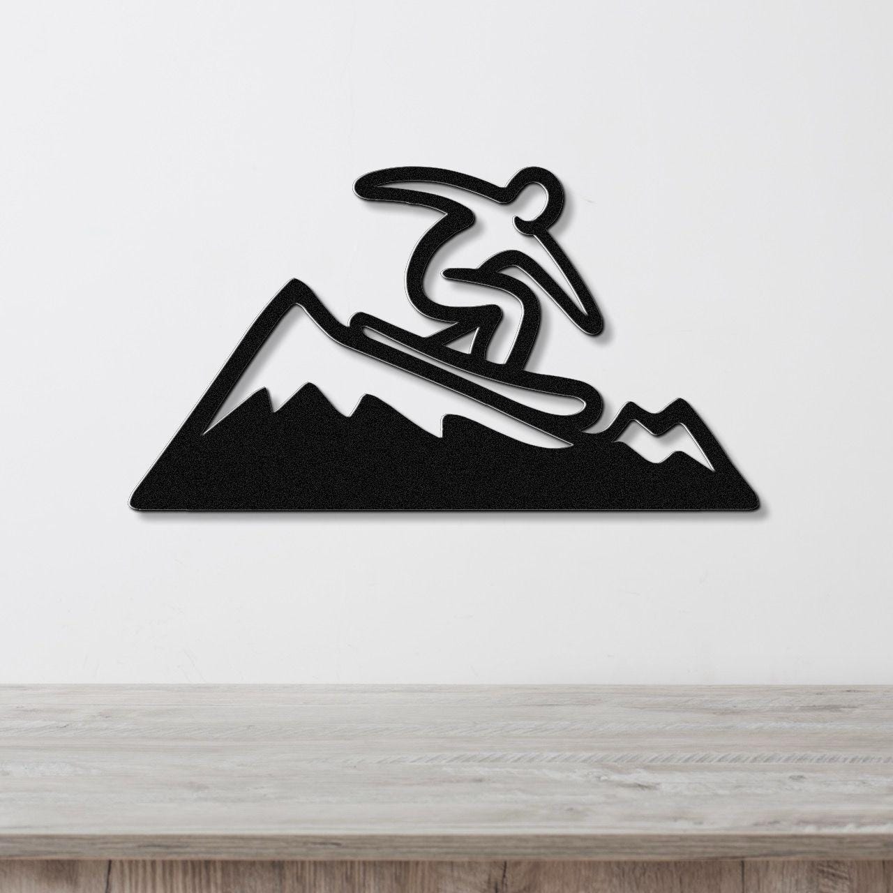 Black metal wall art featuring a snowboarder silhouette in dynamic motion above a mountain range, mounted on a white wall above a wooden counter.