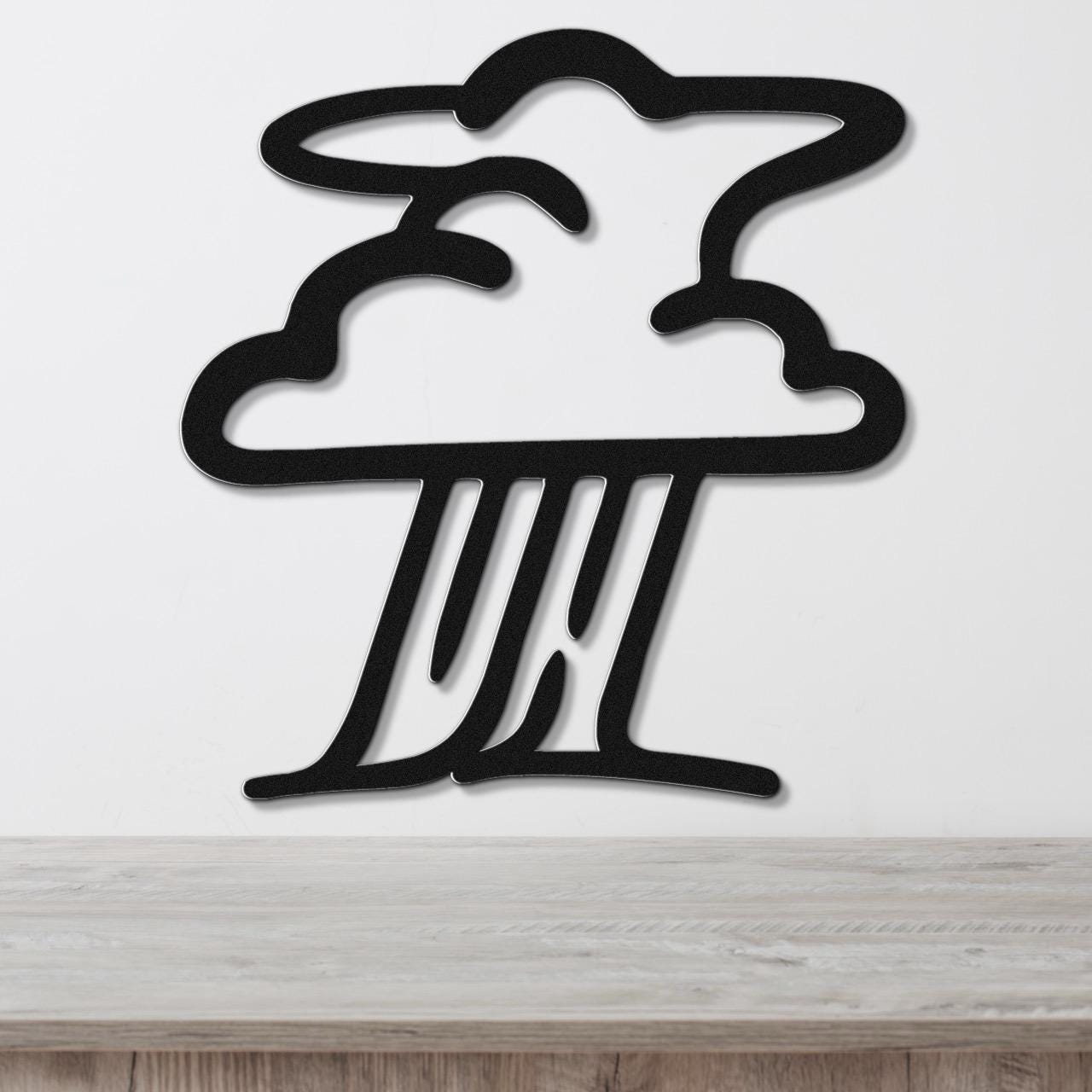 Black metal wall art in a storm cloud silhouette with raindrop cutouts, mounted on a white wall above a light wood surface.