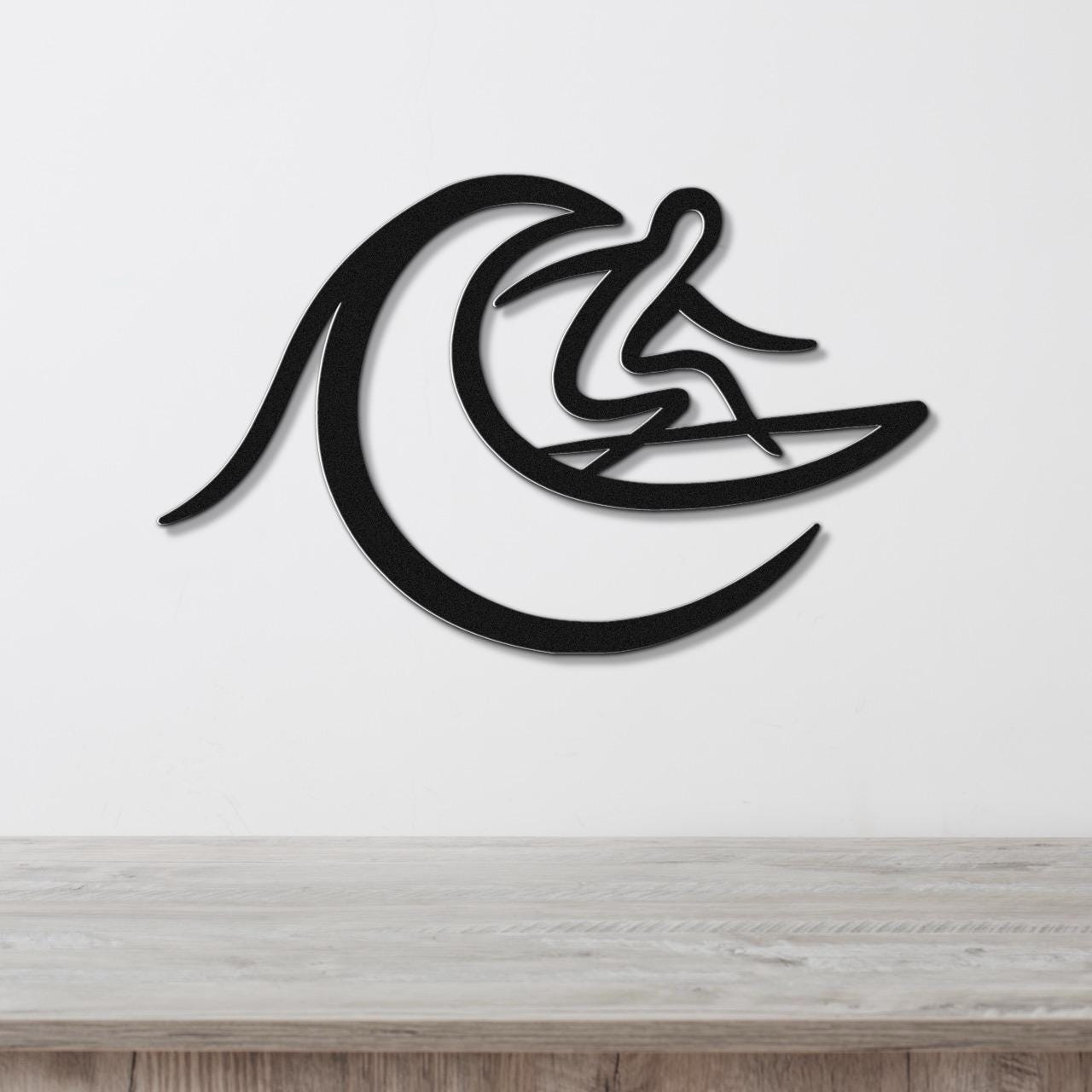Black metal wall art featuring a surfer silhouette riding a wave, mounted on a white wall above a light wood surface.