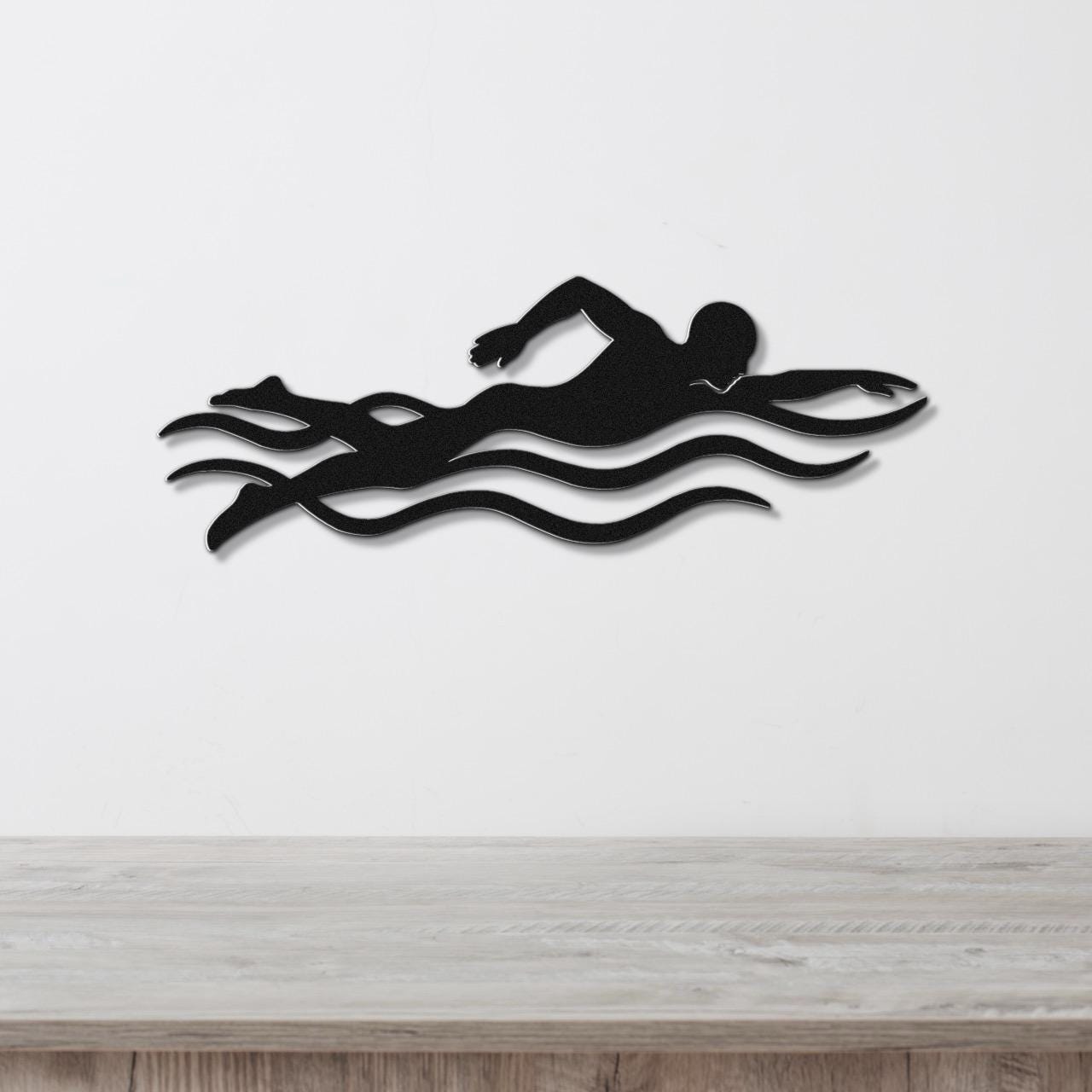 Black metal swimmer wall art with motion-line cutouts, mounted on a white wall above a wooden surface.
