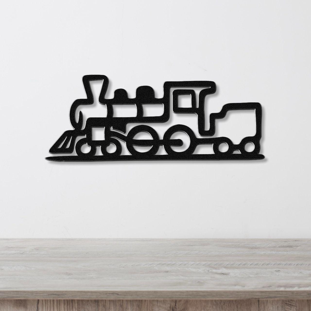 Black metal train wall art with a bold silhouette design and internal cutouts, mounted on a white wall above a light wood surface.