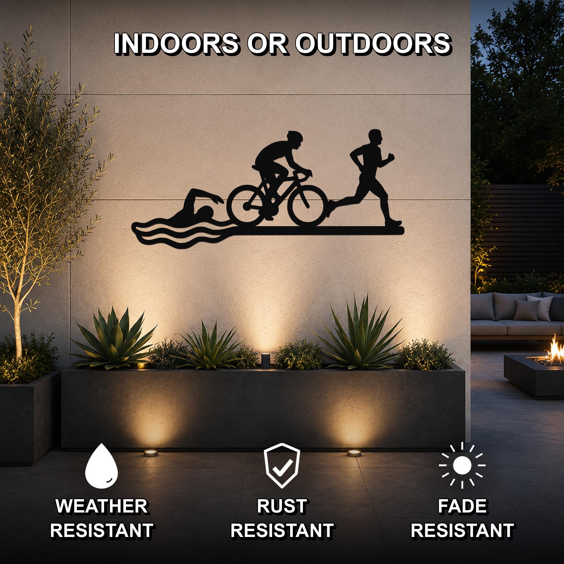 Black metal triathlon wall art with swim, bike, and run silhouettes, mounted on an outdoor wall above a planter in a modern patio setting.