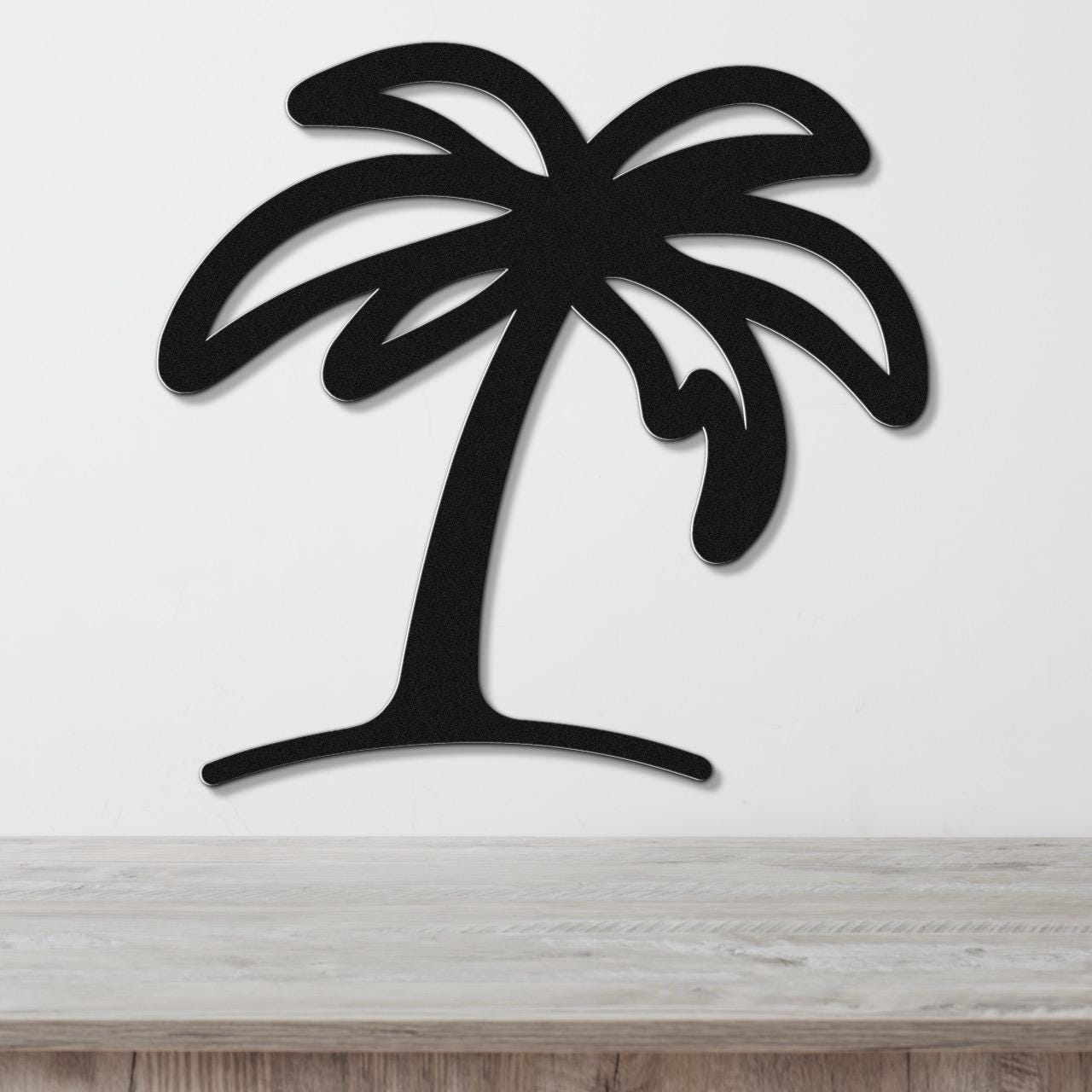 Black metal palm tree wall art with leaf cutouts, mounted on a white wall above a light wood surface.