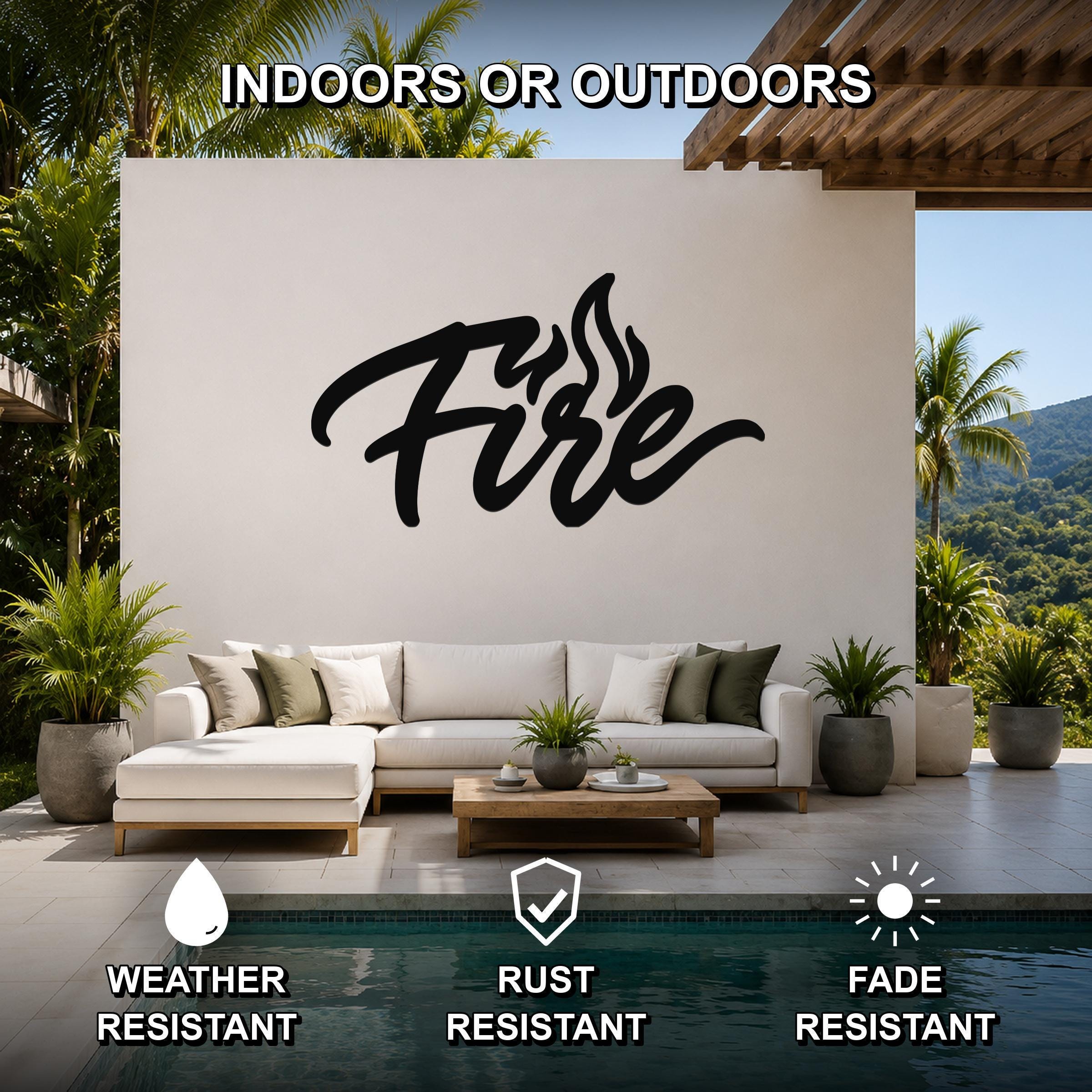 Black metal wall sculpture with the word "Fire" in cursive script and flame cutouts, mounted on a white outdoor wall above a sofa in a patio living area.