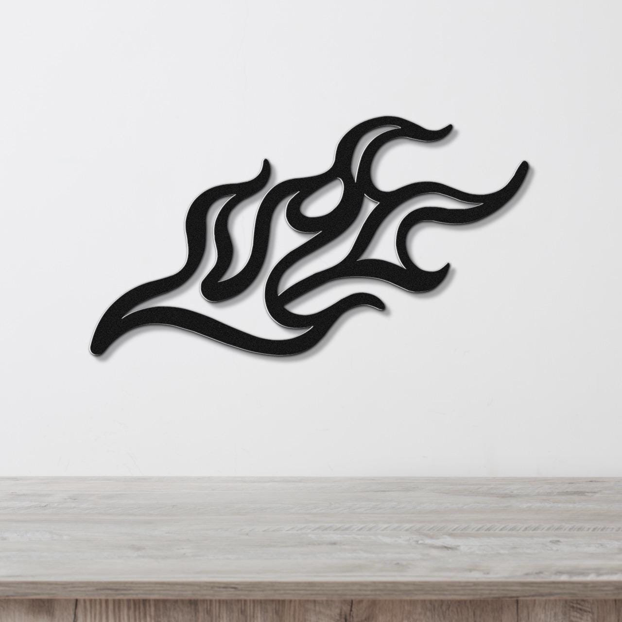 Black metal wall art with a fluid flame design, featuring interwoven curves and cutouts, mounted on a white wall above a light wood surface.