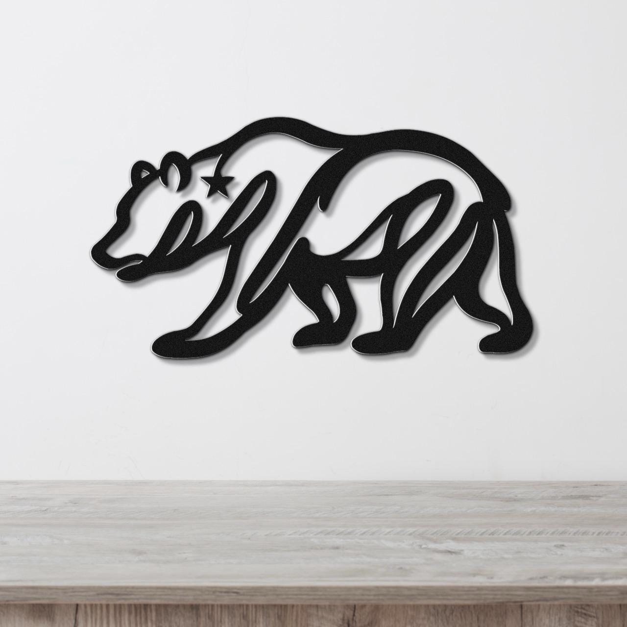 Black metal wall art of a bear silhouette with a star cutout on its shoulder, mounted on a white wall above a wooden surface.