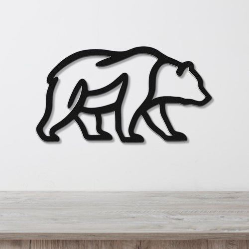 Black metal bear silhouette wall art with internal cutout details, mounted on a white wall above a light wood surface.