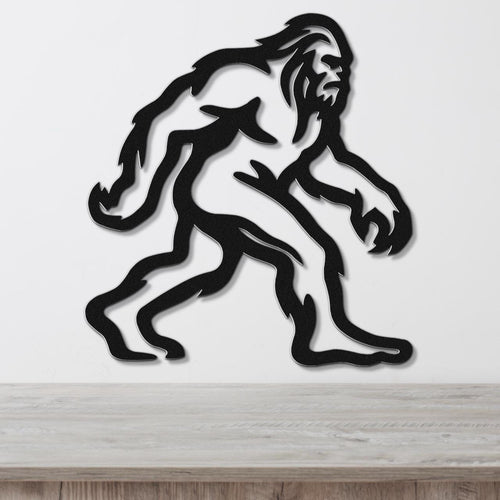 Black metal wall art featuring a rugged Bigfoot silhouette with internal cutout details, mounted on a white wall above a wooden surface.