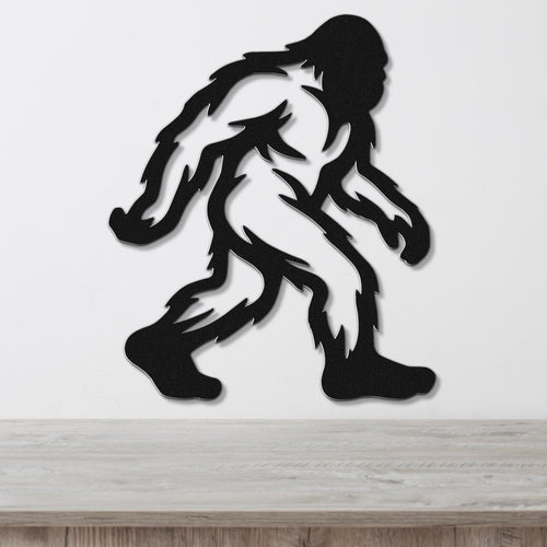 Black metal Bigfoot wall art silhouette with internal cutout details, mounted on a white wall above a wooden surface.