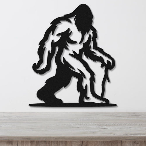 Black metal wall art silhouette of Bigfoot with detailed fur cutouts, mounted on a white wall above a wooden surface.