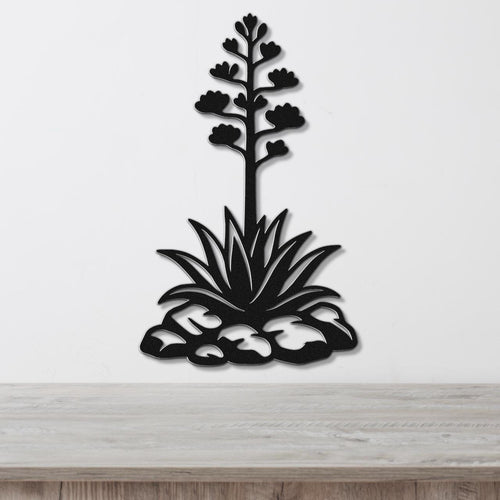 Black metal agave wall sculpture with blooming flower stalk and spiky leaves, mounted on a white wall above a wooden surface.