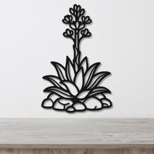 Black metal agave wall art with blooming flower cutout, mounted on a white wall above a wooden surface.
