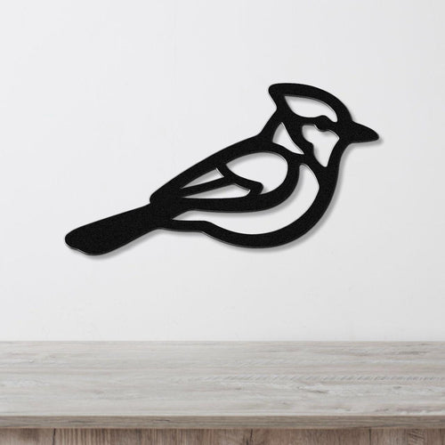 Black metal wall art featuring a cutout silhouette of a blue jay with internal detail, mounted on a white wall above a light wood surface.