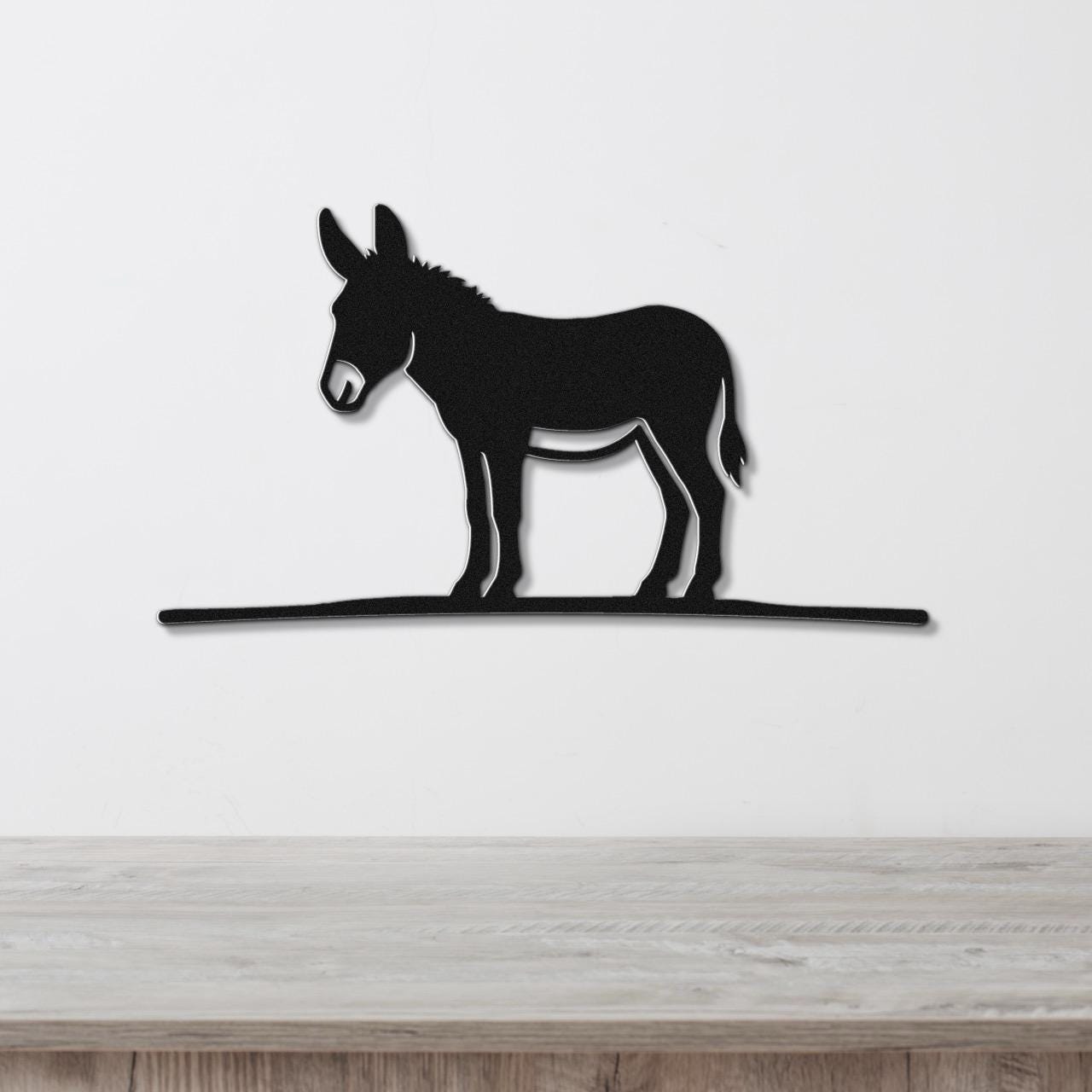 Black metal donkey wall art silhouette with a long horizontal base, mounted on a white wall above a wooden surface.