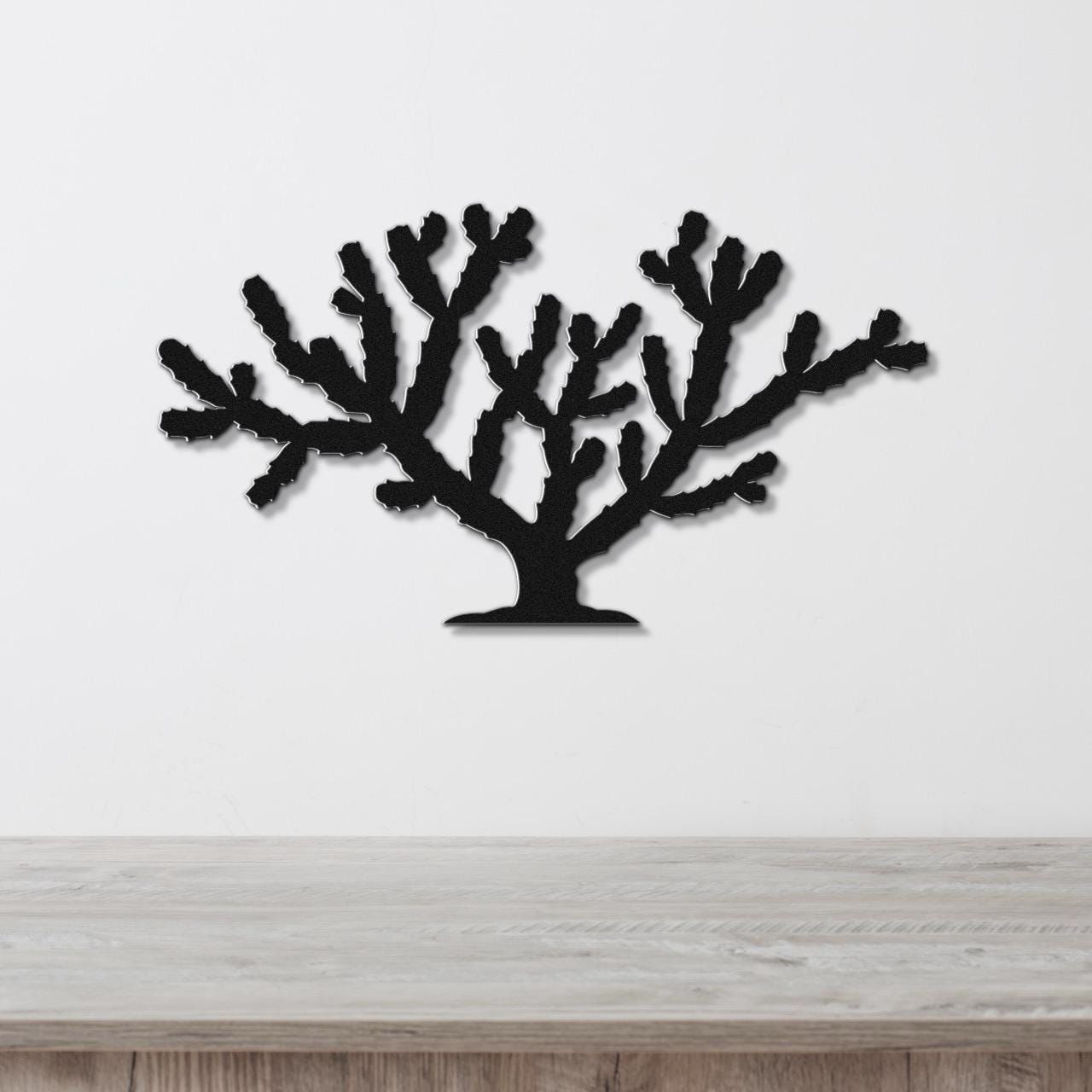 Black metal wall art cutout of a cholla cactus with branching arms, mounted on a white wall above a light wood surface.