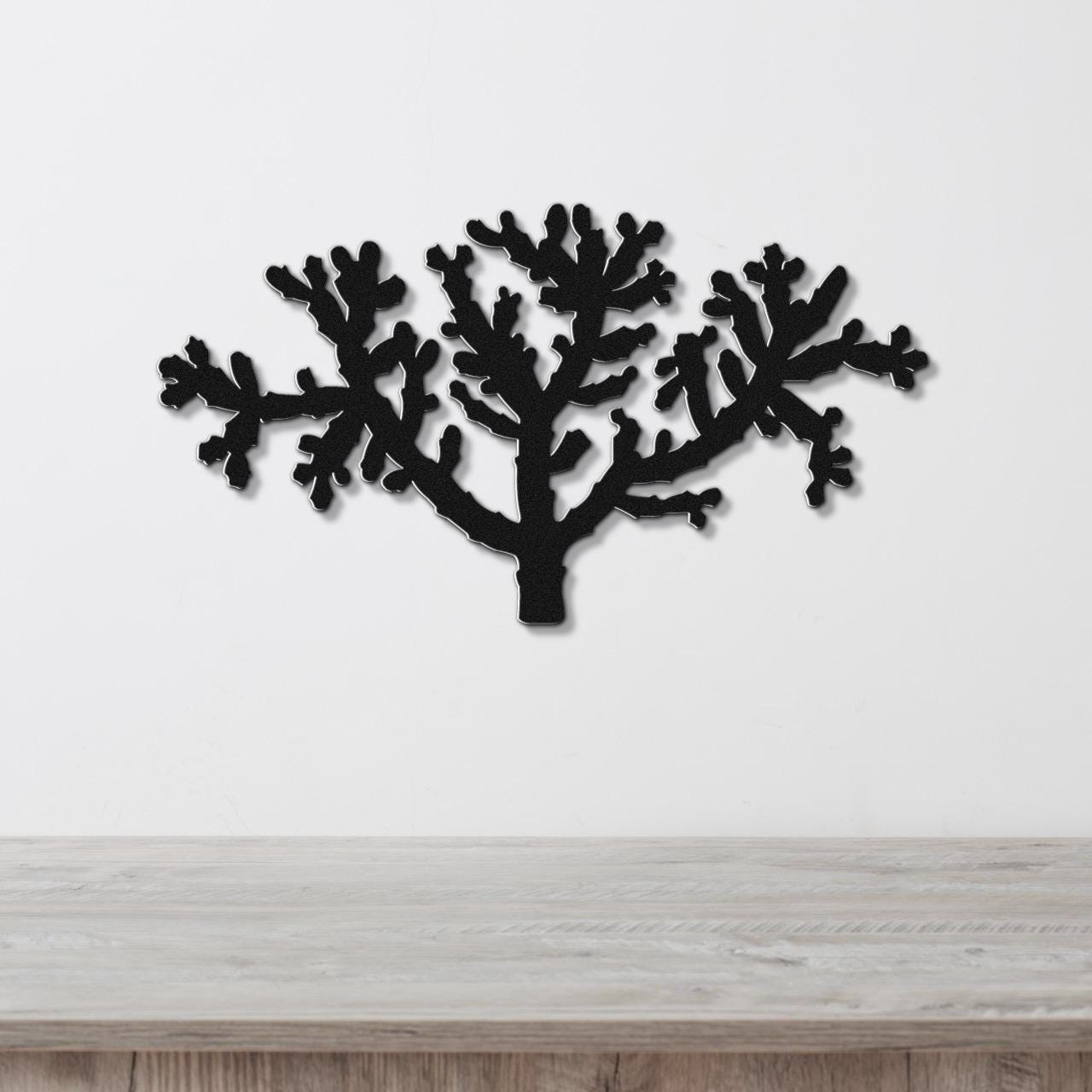 Black metal wall art cutout of a cholla cactus with branching arms, mounted on a white wall above a light wood surface.