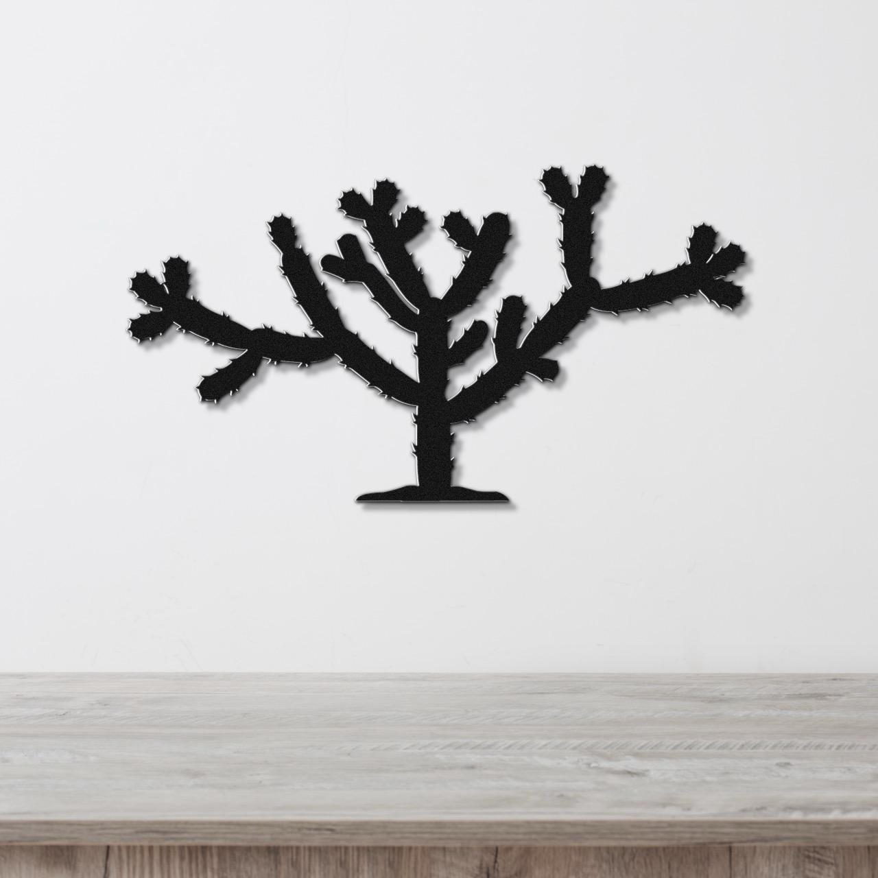 Black metal Cholla cactus wall art with spiky branch cutouts, mounted on a white wall above a light wood counter.