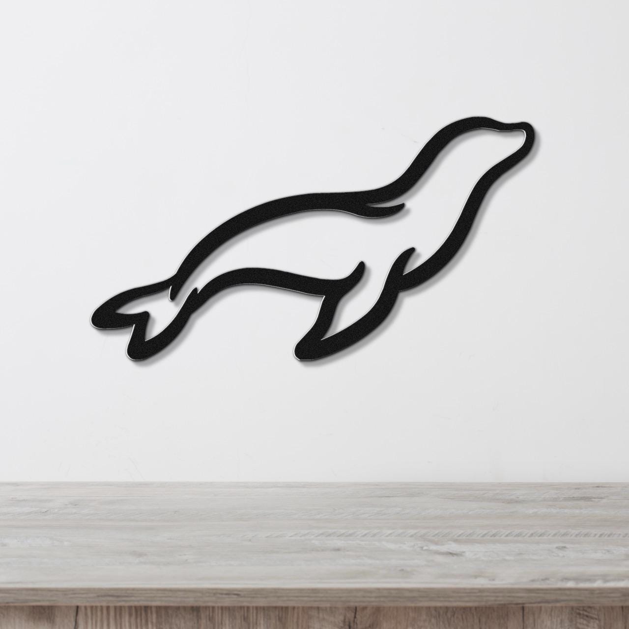 Black metal sea lion wall art with a sleek silhouette design, mounted on a white wall above a light wood surface.