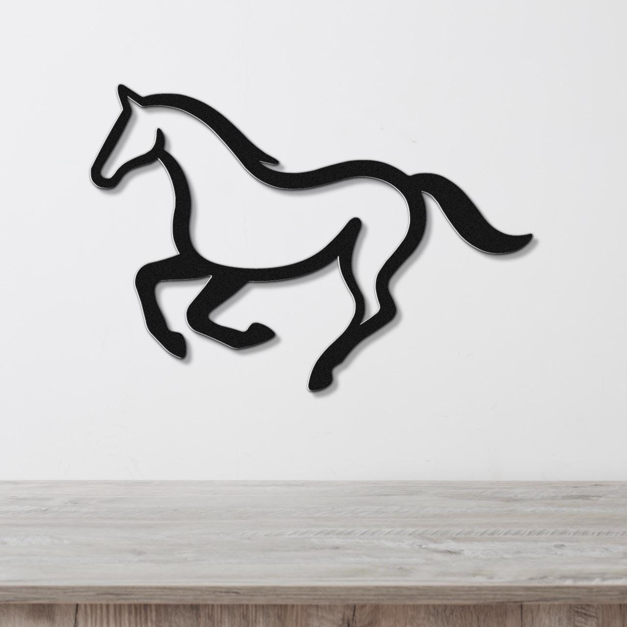 Black metal horse wall art in a running silhouette, mounted on a white wall above a light wood counter.