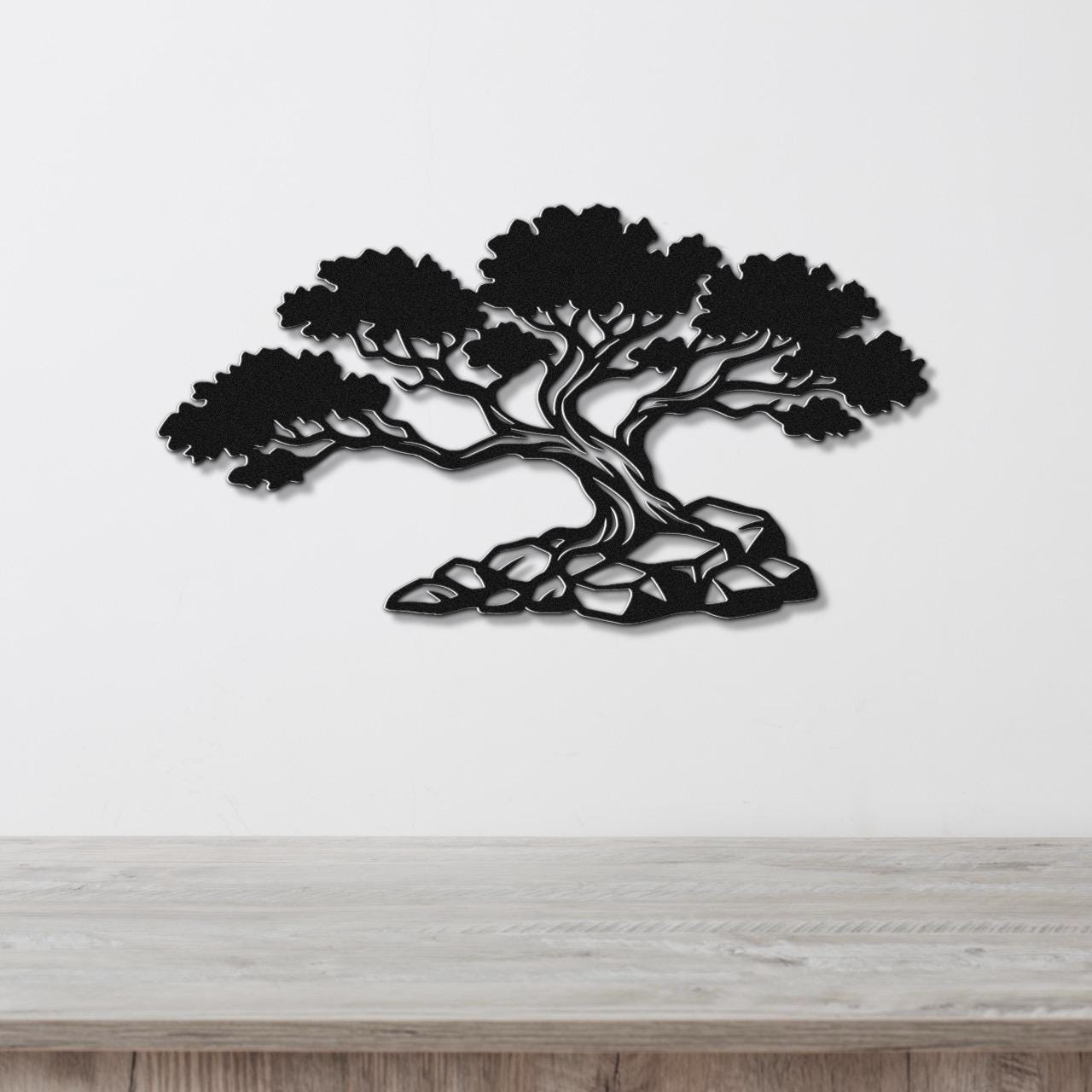 Black metal wall art cutout of a juniper tree with detailed branches and roots, mounted on a white wall above a wooden surface.