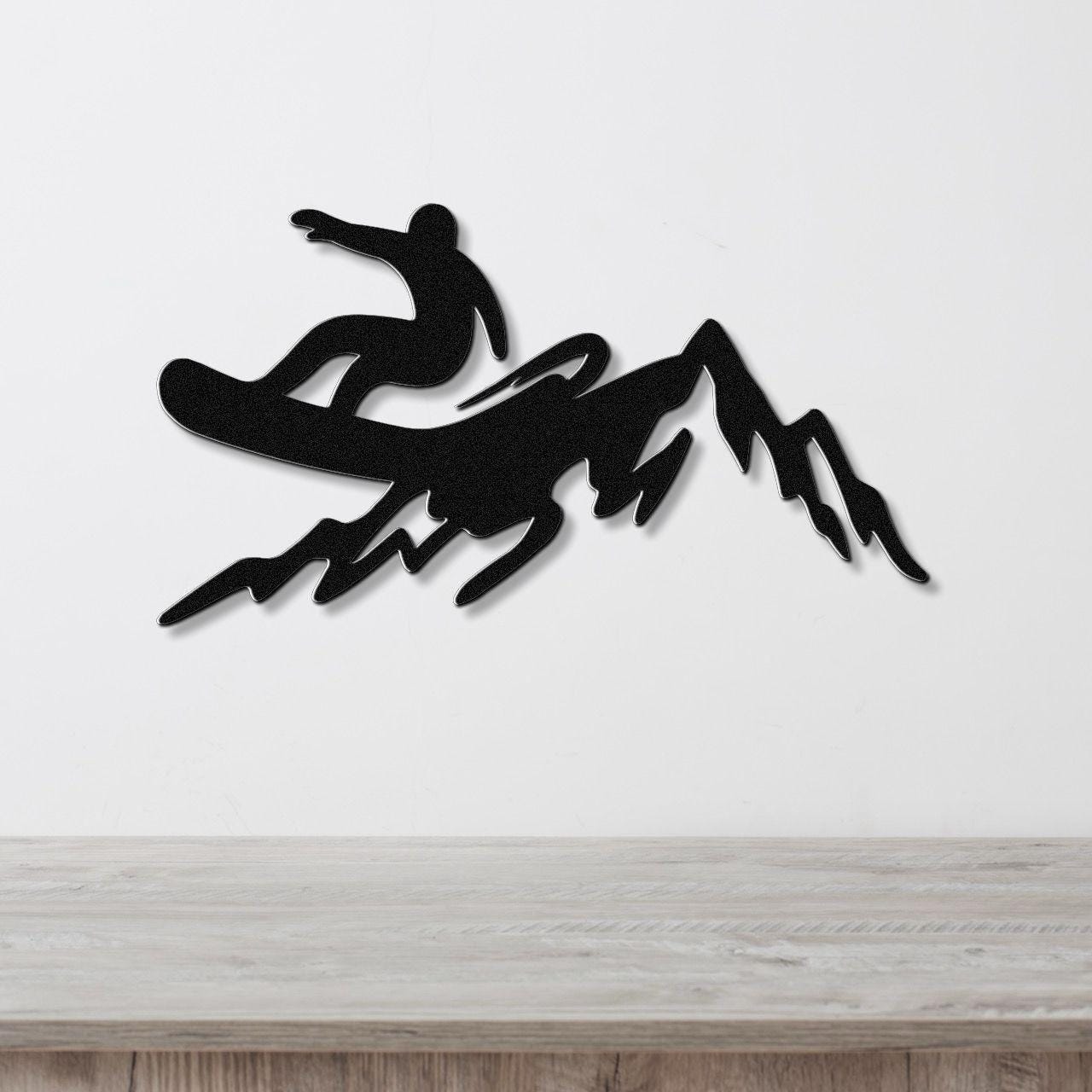 Black metal wall art silhouette of a snowboarder in mid-air above a mountain range, mounted on a white wall above a light wood counter.