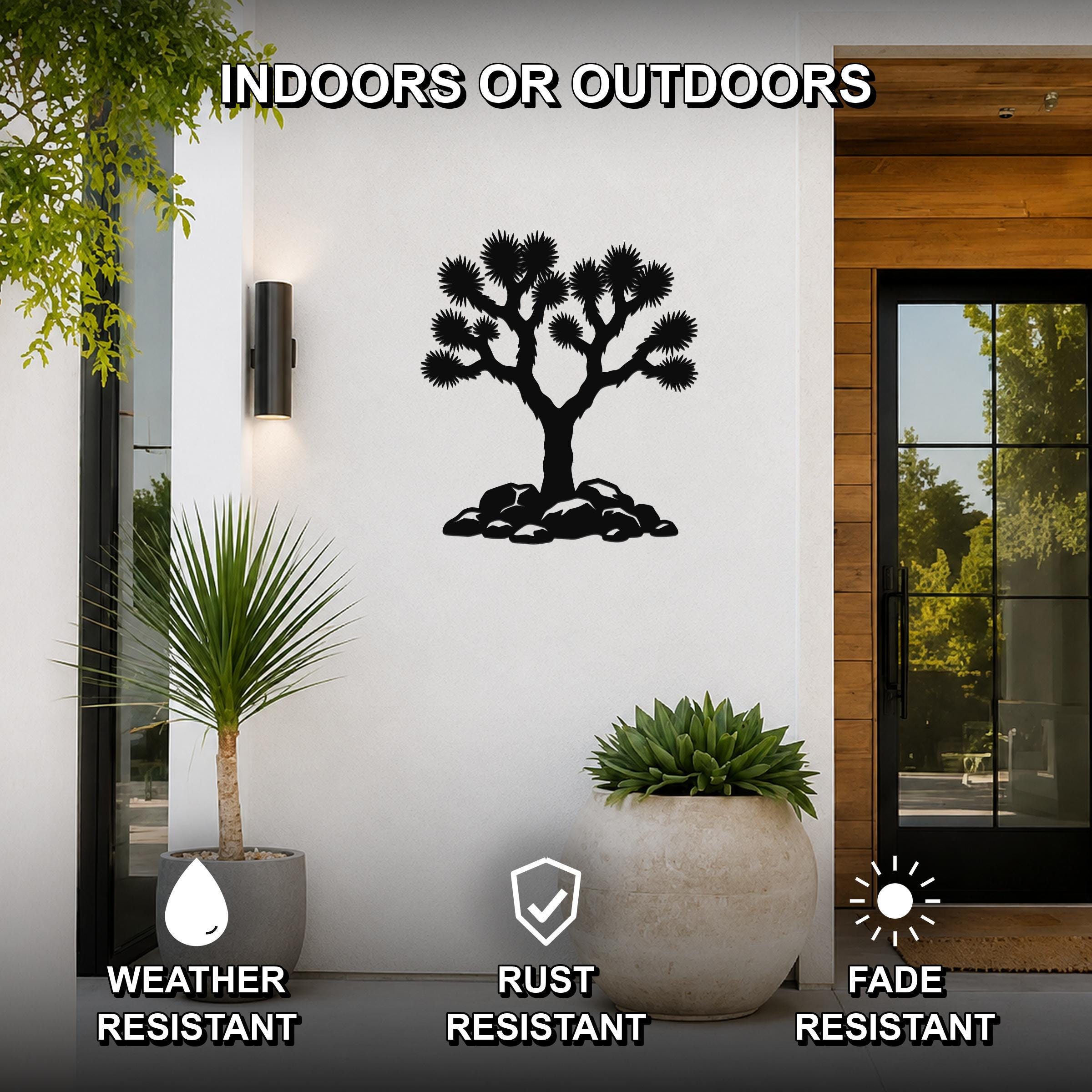 Black metal Joshua tree wall art with branch and rock cutouts, mounted on a white exterior wall beside a glass door and potted plants.
