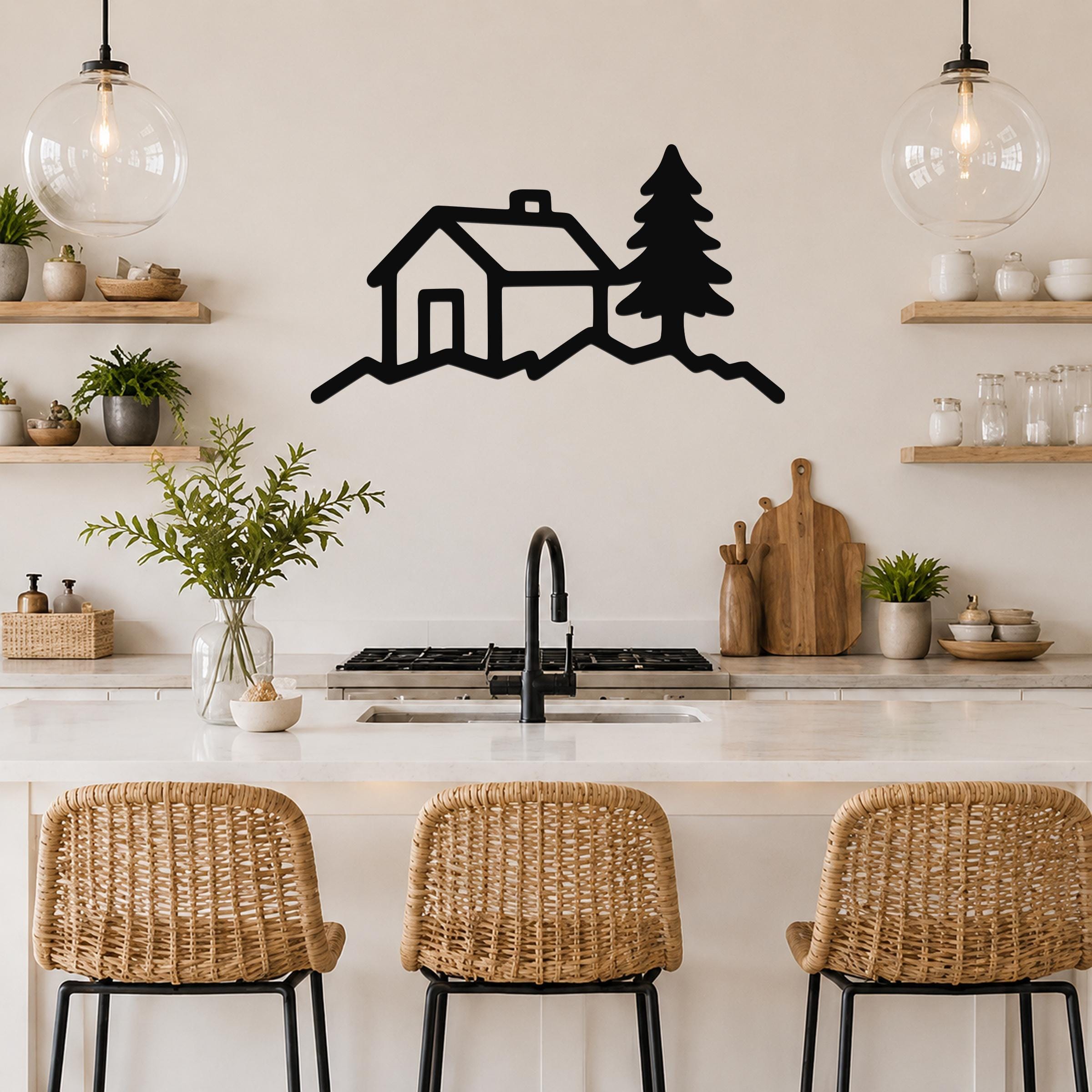 Black metal wall art silhouette of a cabin and pine tree, mounted on a kitchen wall above a counter with wicker bar stools.
