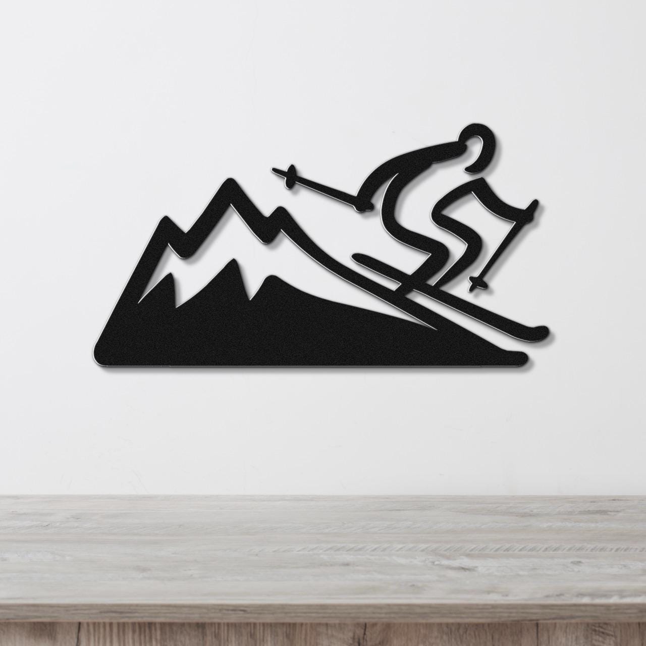 Black metal wall sculpture of a skier descending a mountain, mounted on a white wall above a wooden surface.