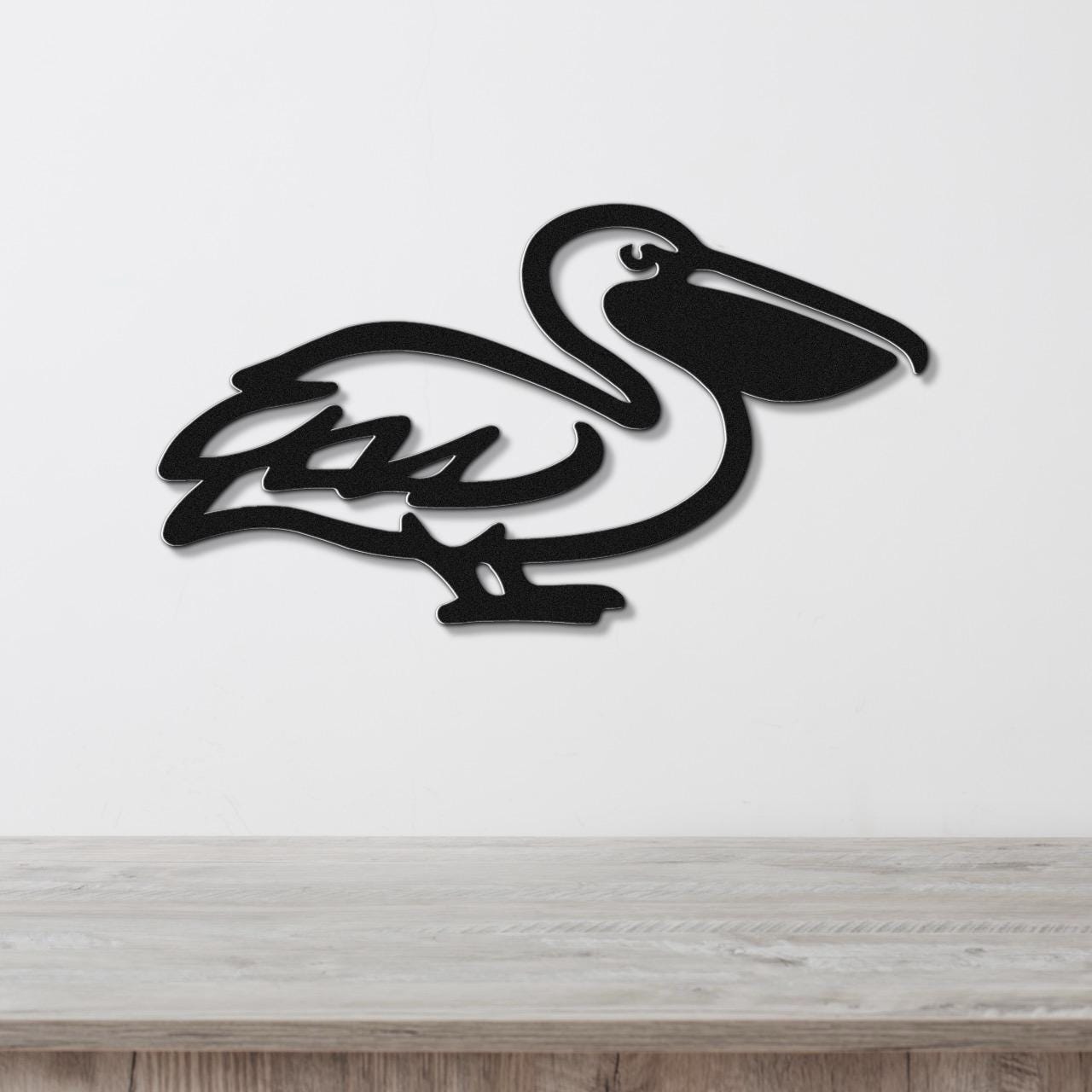 Black metal pelican wall art with a cutout silhouette design, mounted on a white wall above a light wood surface.