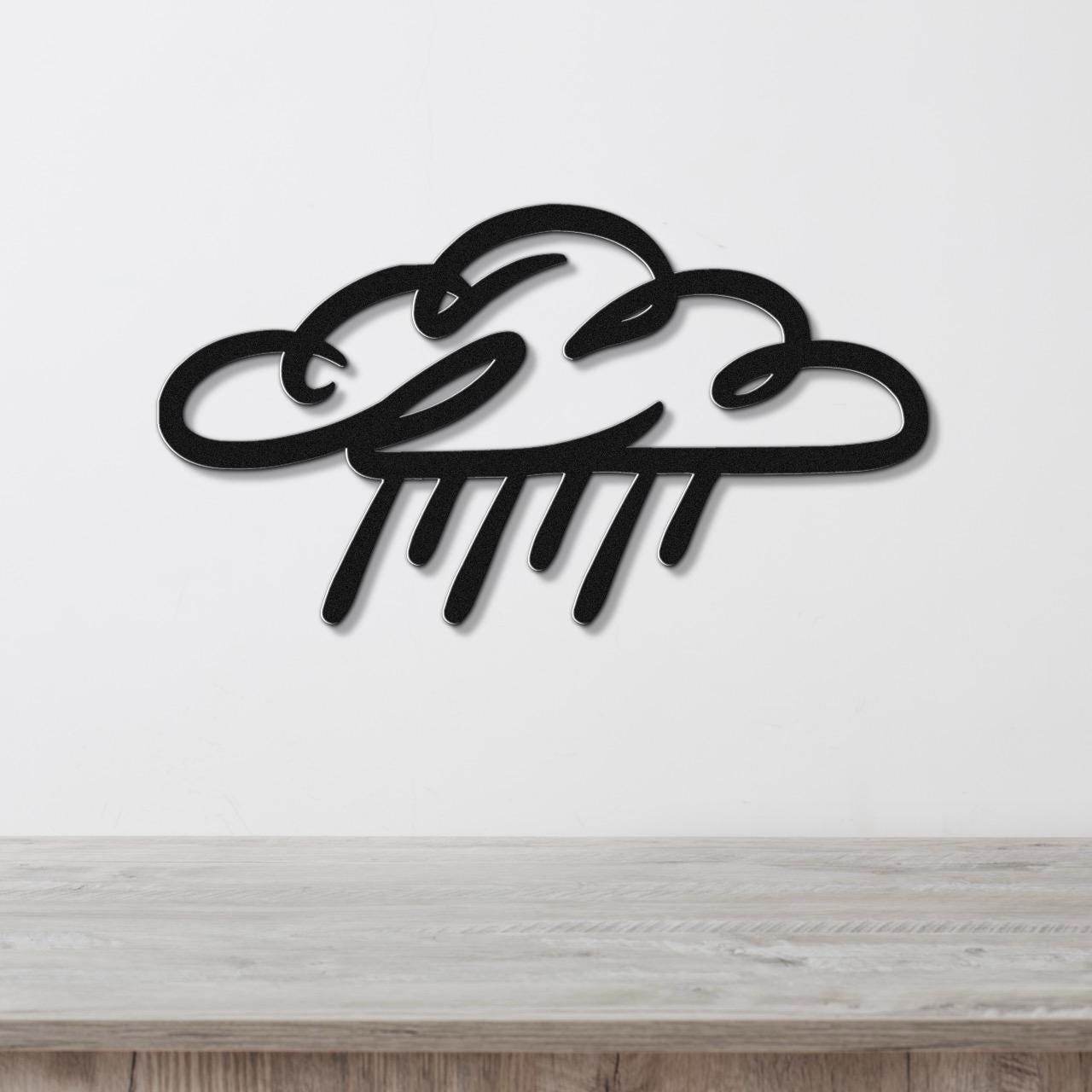 Black metal wall art in a cloud and raindrop silhouette design, mounted on a white wall above a light wood surface.