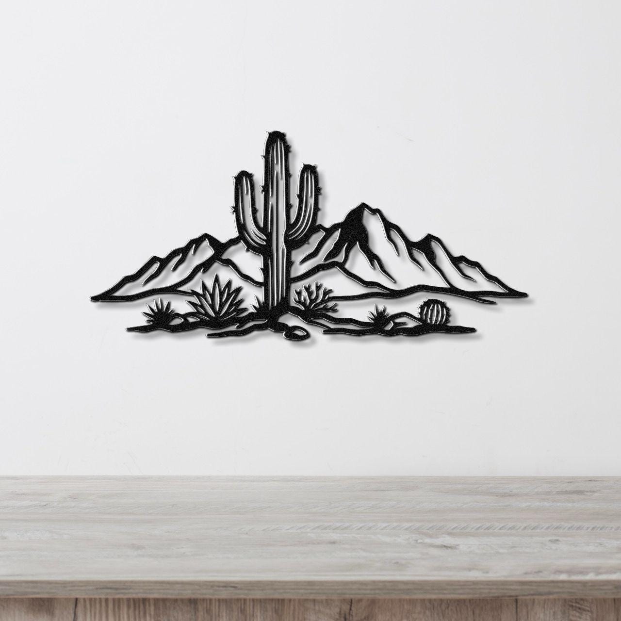 Black metal wall art silhouette of a saguaro cactus and desert landscape with mountains and smaller cacti, mounted on a white wall above a light wood surface.