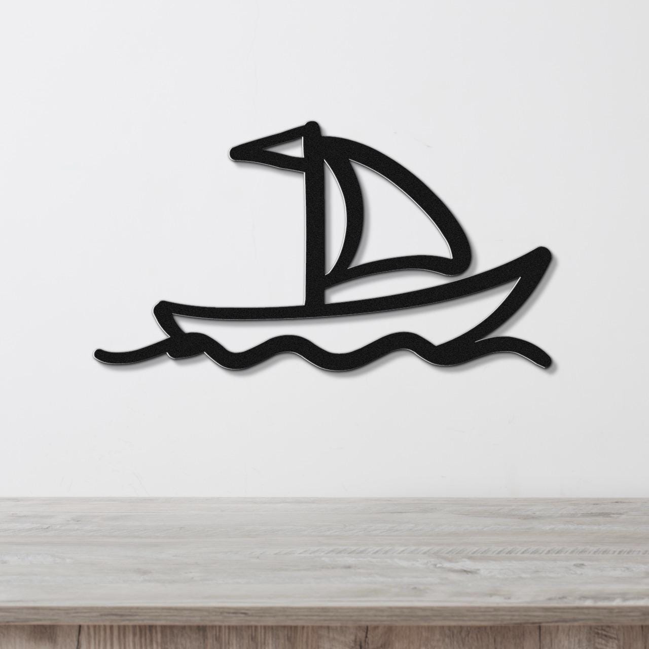 Black metal sailboat wall art with wave cutouts, mounted on a white wall above a light wood surface.